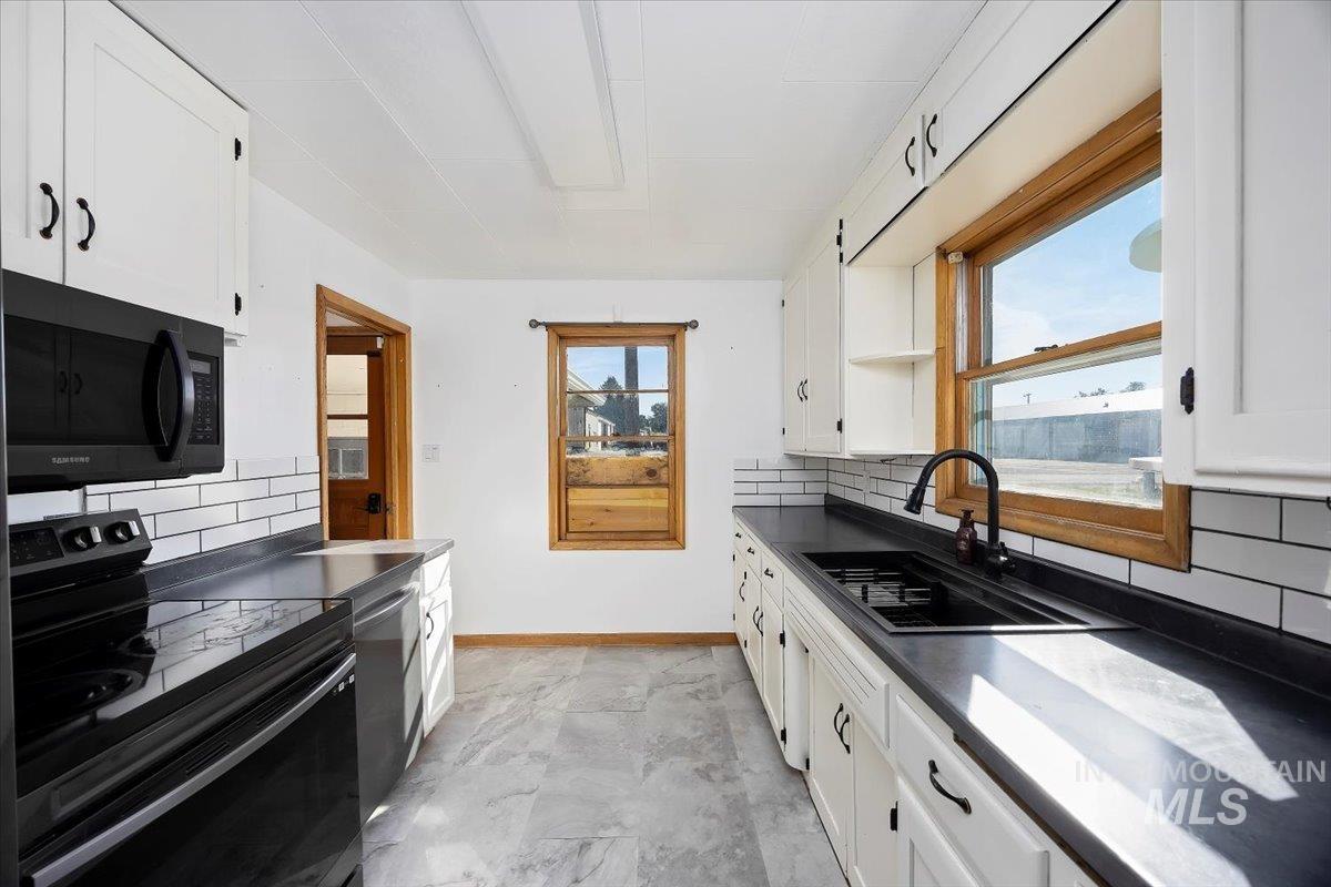 Kitchen featuring electric stove, dark countertops, backsplash, black microwave, and white cabinets