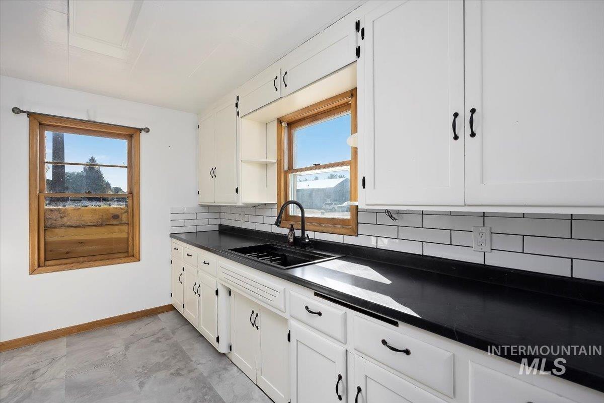 Kitchen with tasteful backsplash, dark countertops, plenty of natural light, and white cabinetry