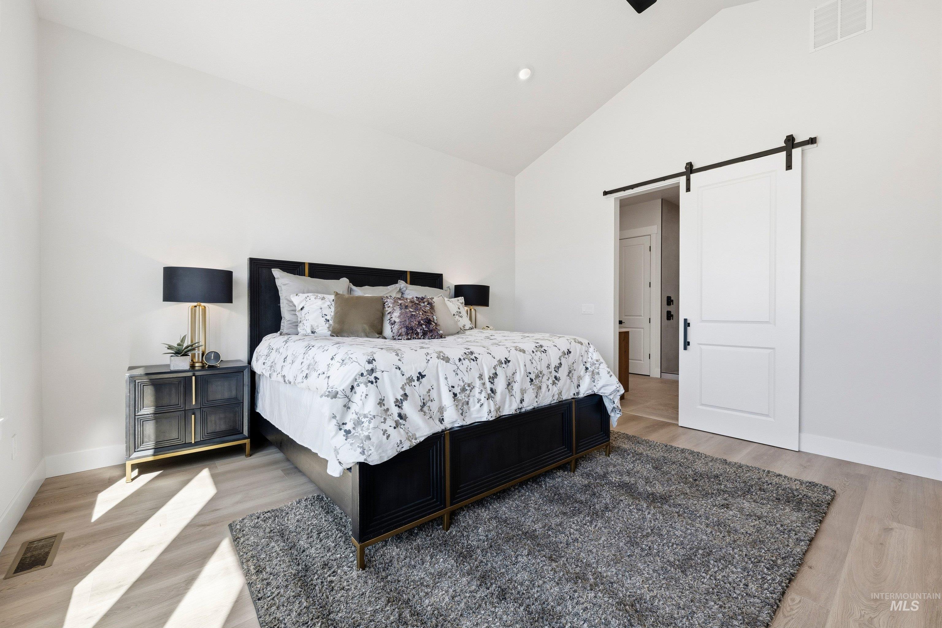 Bedroom featuring a barn door, vaulted ceiling, light wood finished floors, recessed lighting, and a ceiling fan