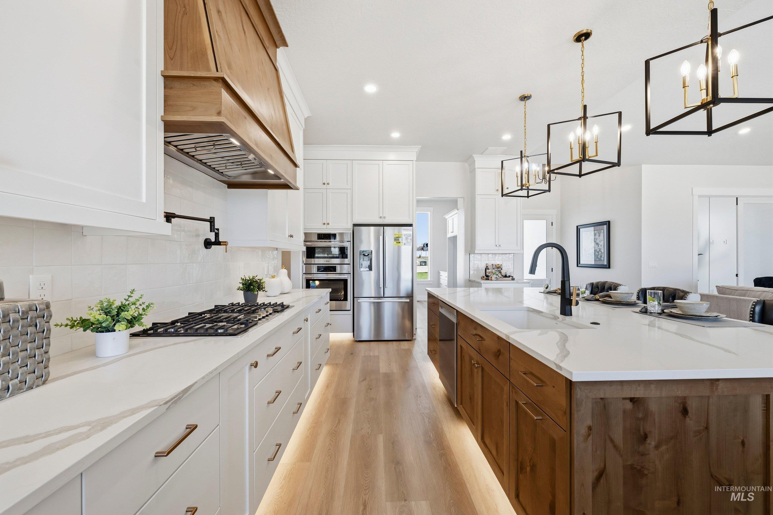 Kitchen featuring two tone cabinetry, light stone countertops, stainless steel appliances, light wood-style flooring, and decorative backsplash