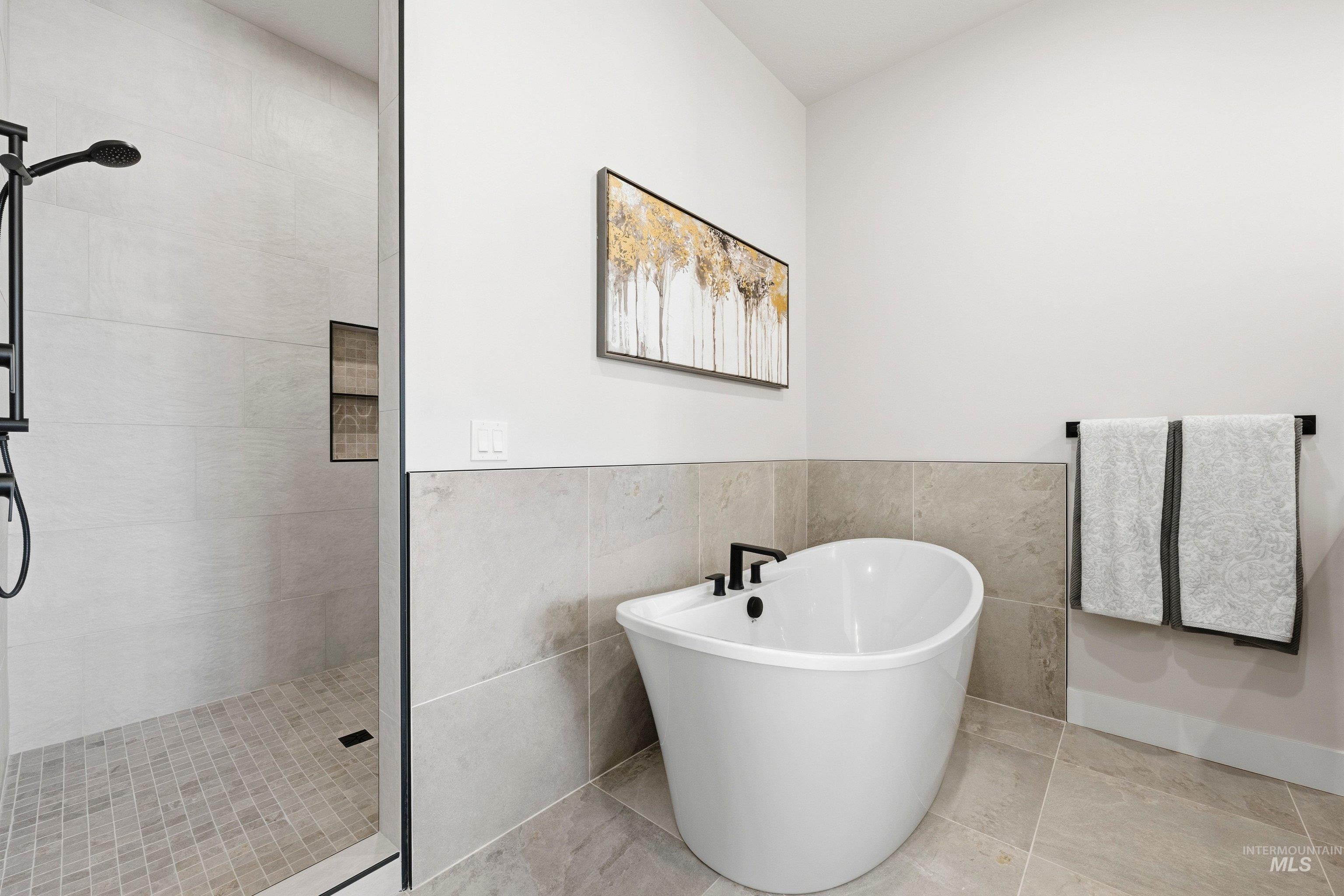 Bathroom with a shower stall, a freestanding tub, tile walls, tile patterned flooring, and wainscoting
