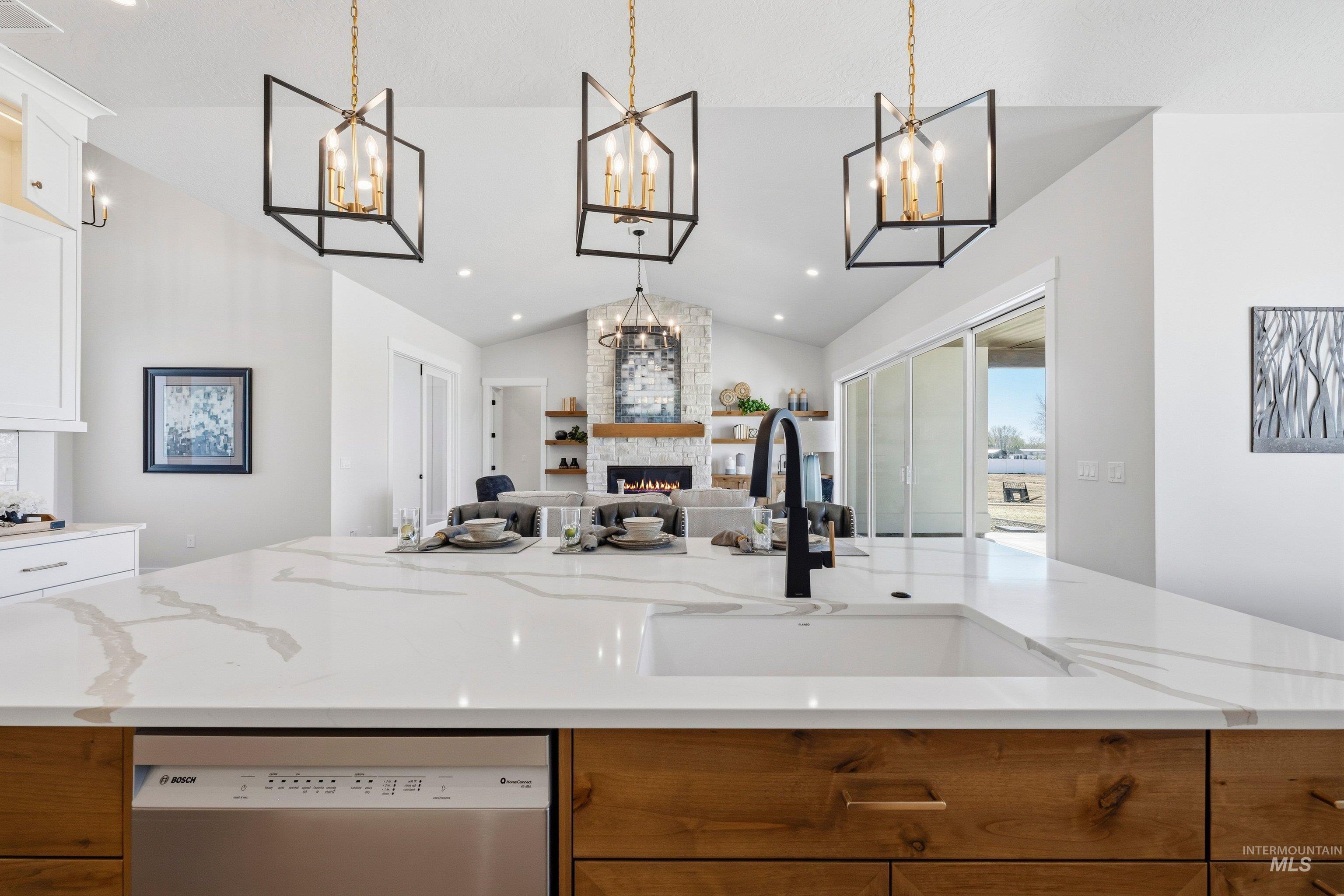 Two tone kitchen featuring a large fireplace, an island with sink, light stone counters, dishwasher, and open floor plan