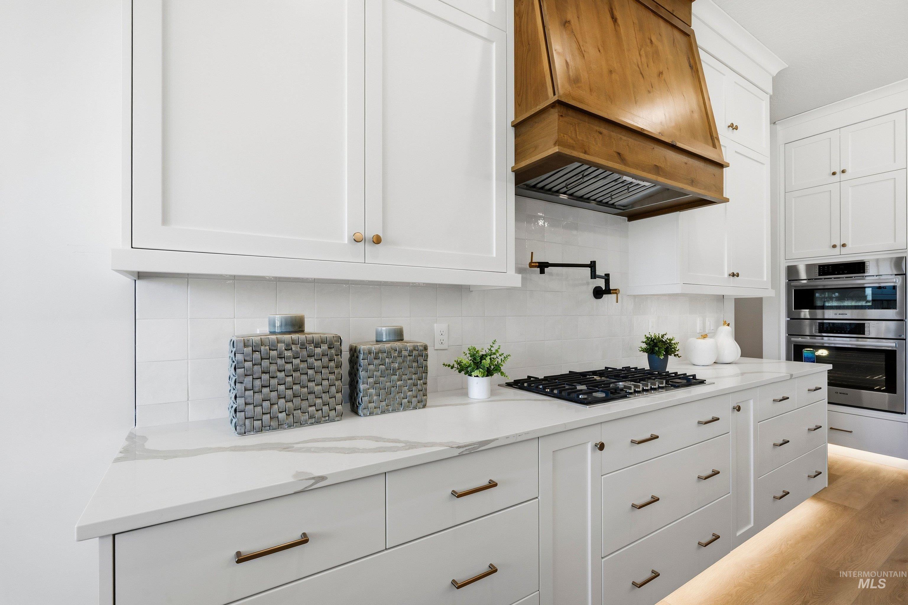 Kitchen with white cabinets, stainless steel appliances, light stone countertops, light wood-style floors, and tasteful backsplash