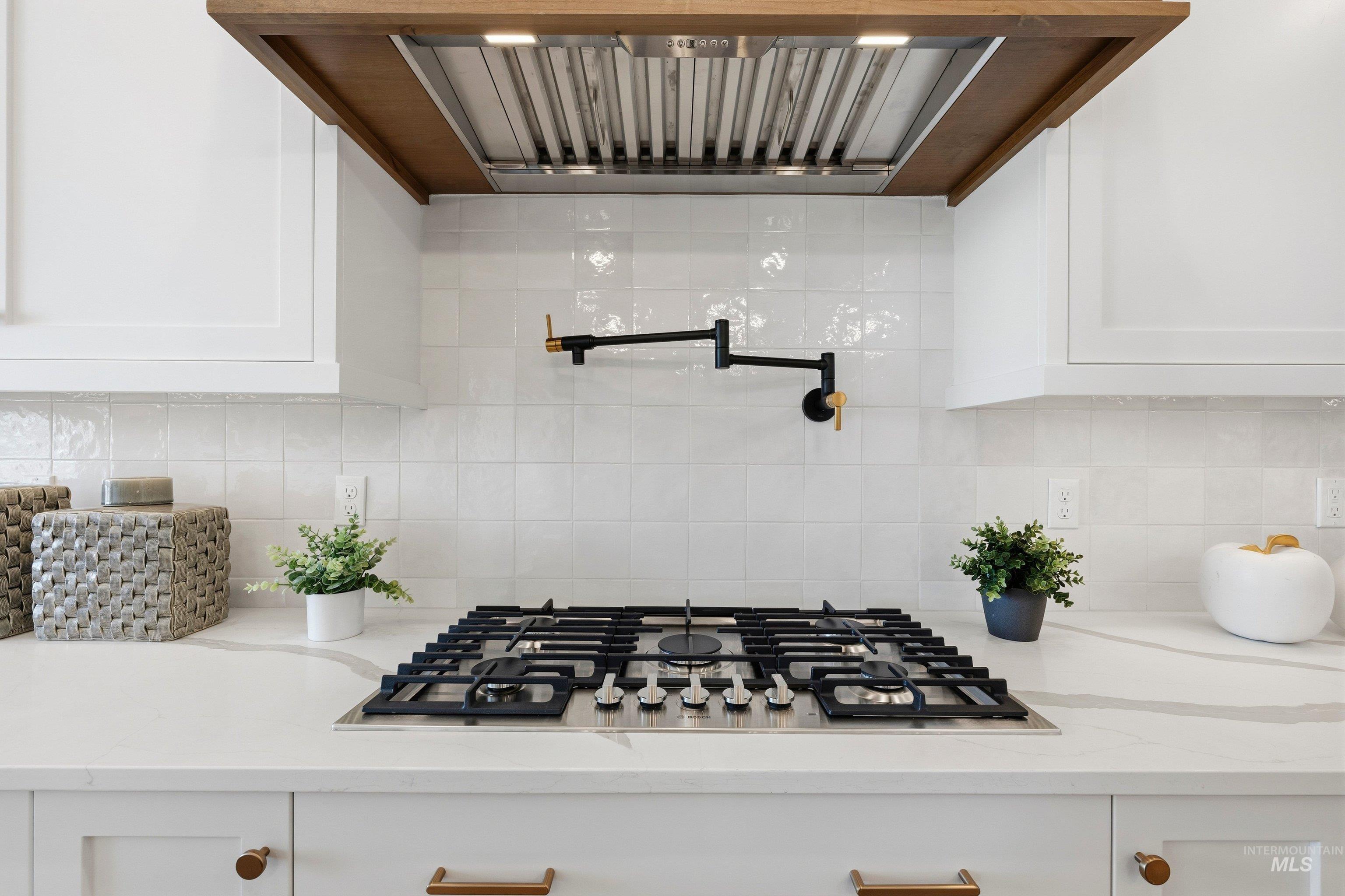 Kitchen featuring ventilation hood, stainless steel gas cooktop, white cabinets, light stone counters, and tasteful backsplash