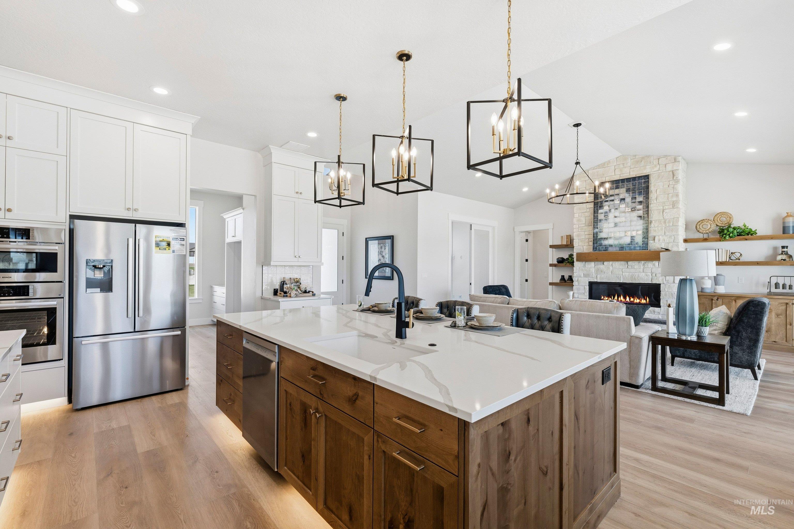 Kitchen featuring dual tone cabinetry, a stone fireplace, stainless steel appliances, open floor plan, and a kitchen island with sink