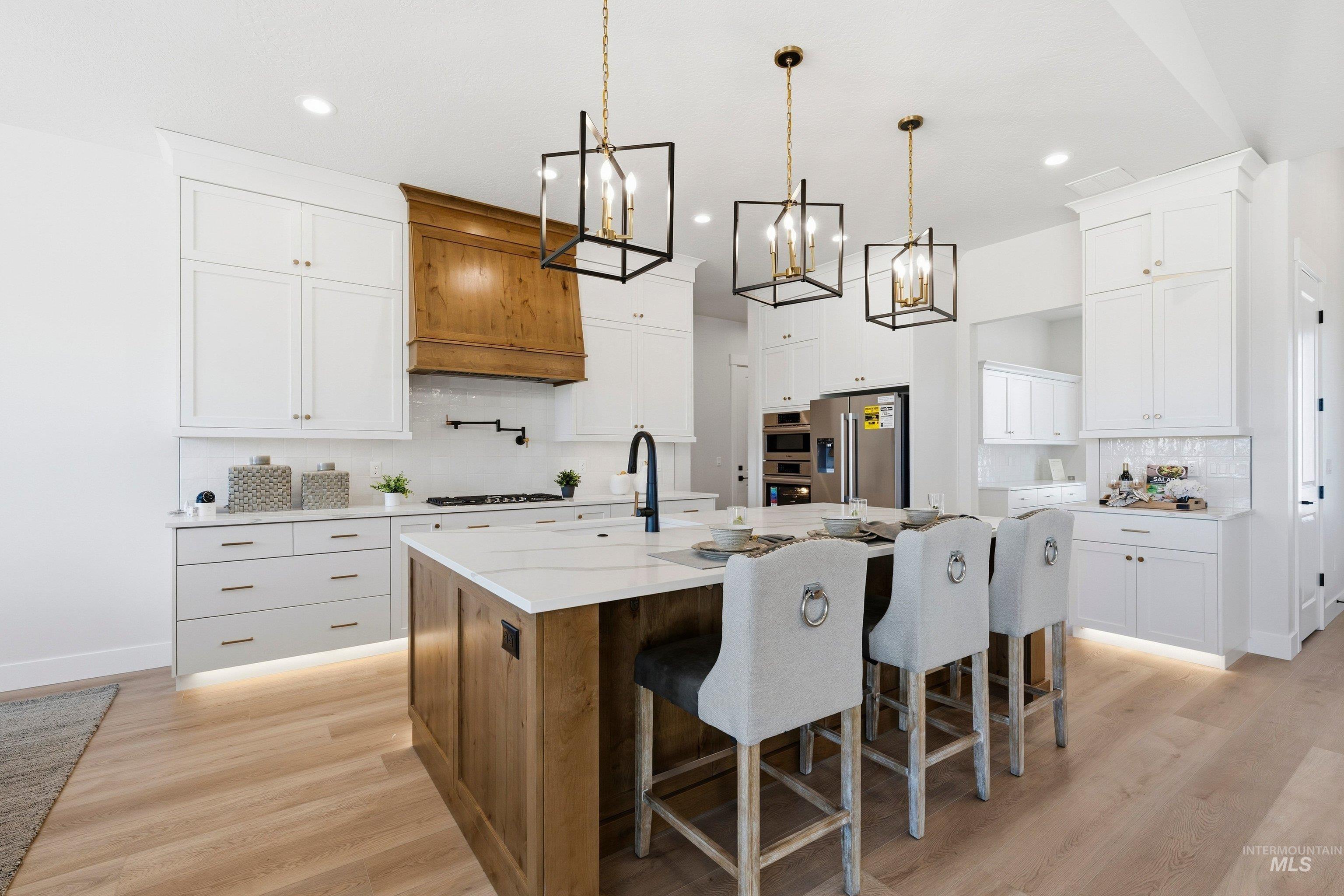 Two tone kitchen featuring dual tone cabinets, hanging lights, decorative backsplash, a kitchen island with sink, and a breakfast bar