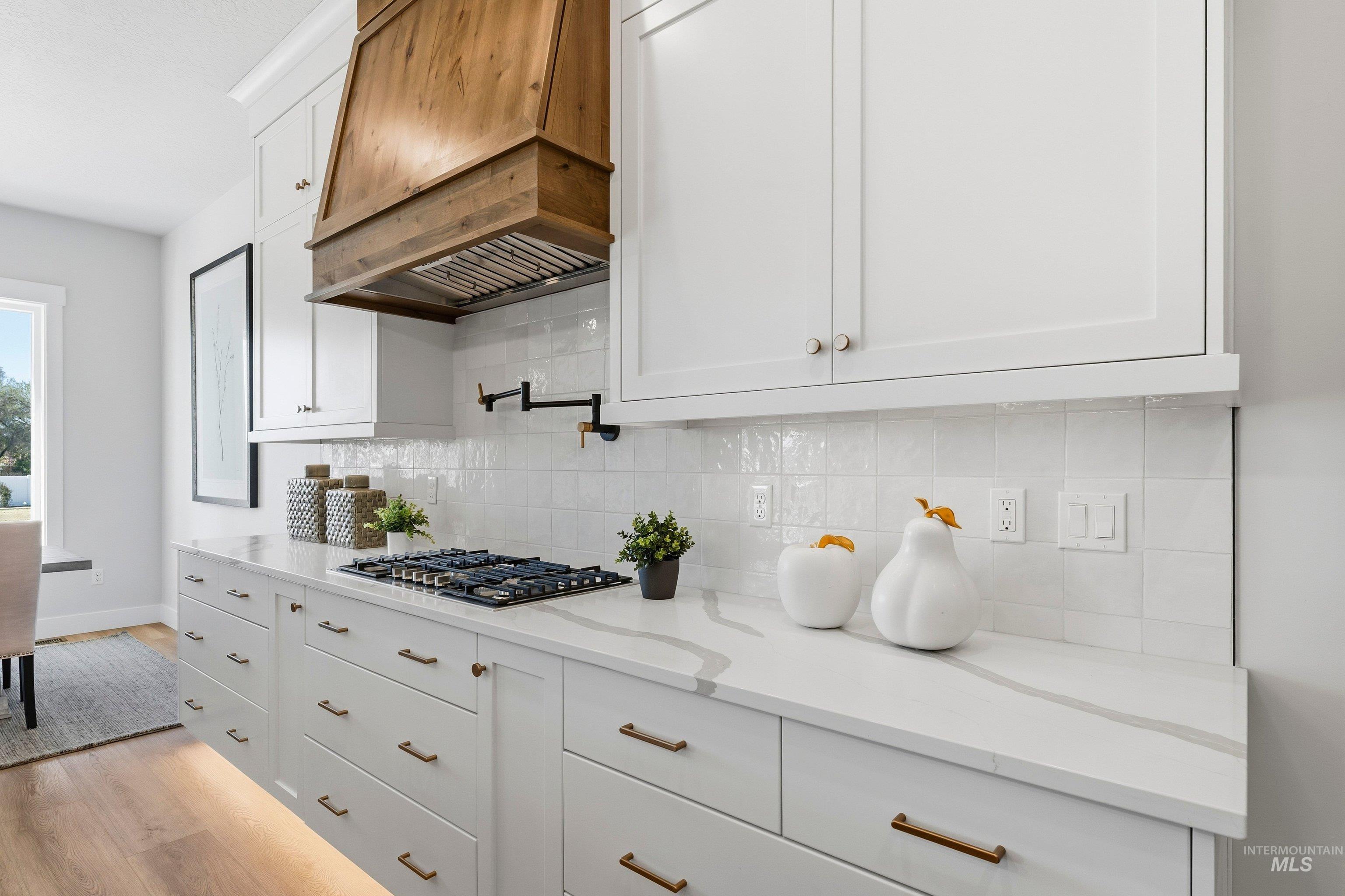 Kitchen with white cabinets, light stone counters, tasteful backsplash, stainless steel gas stovetop, and light wood-style floors
