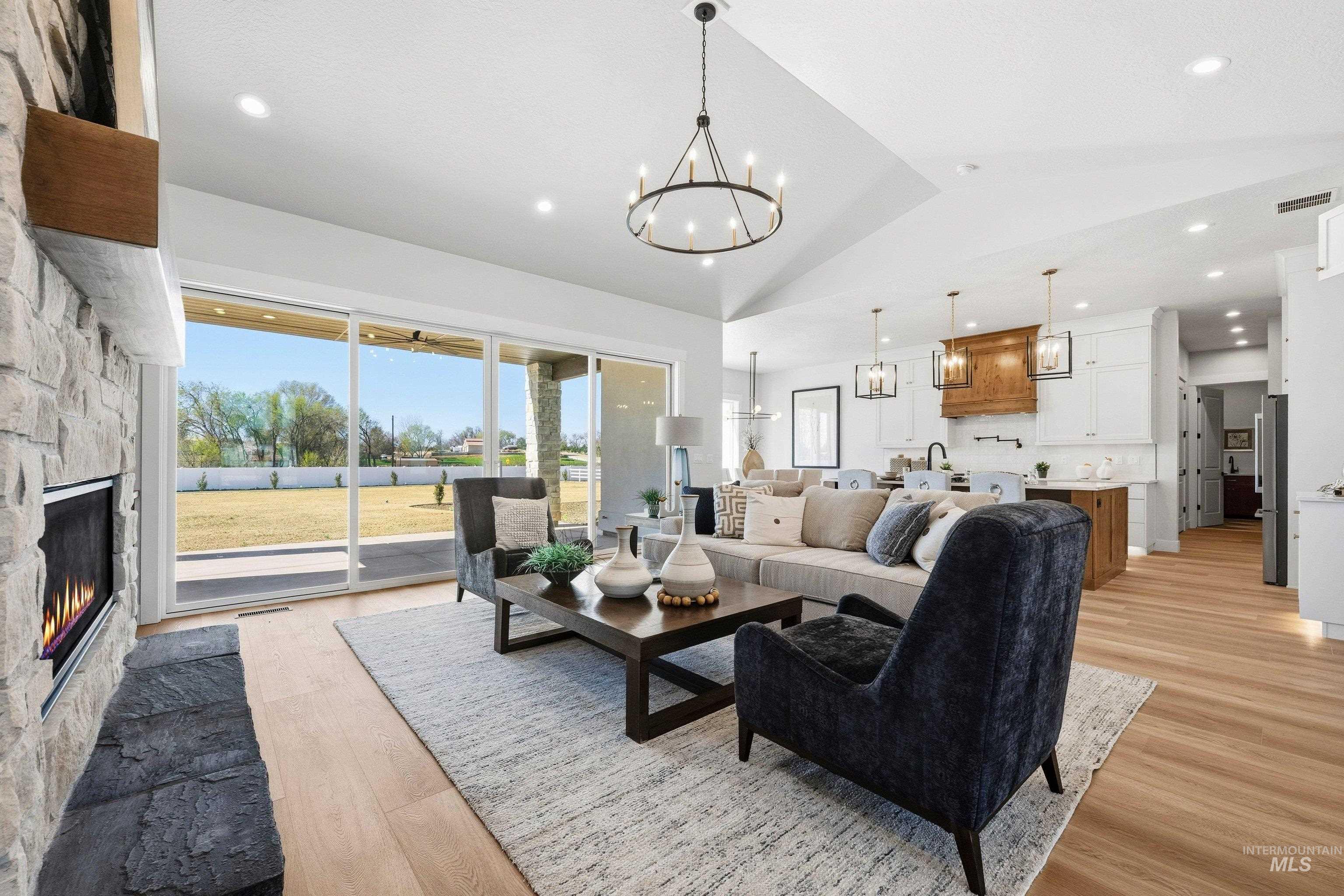 Living room featuring a fireplace, light wood-style flooring, suspended lighting, and lofted ceiling