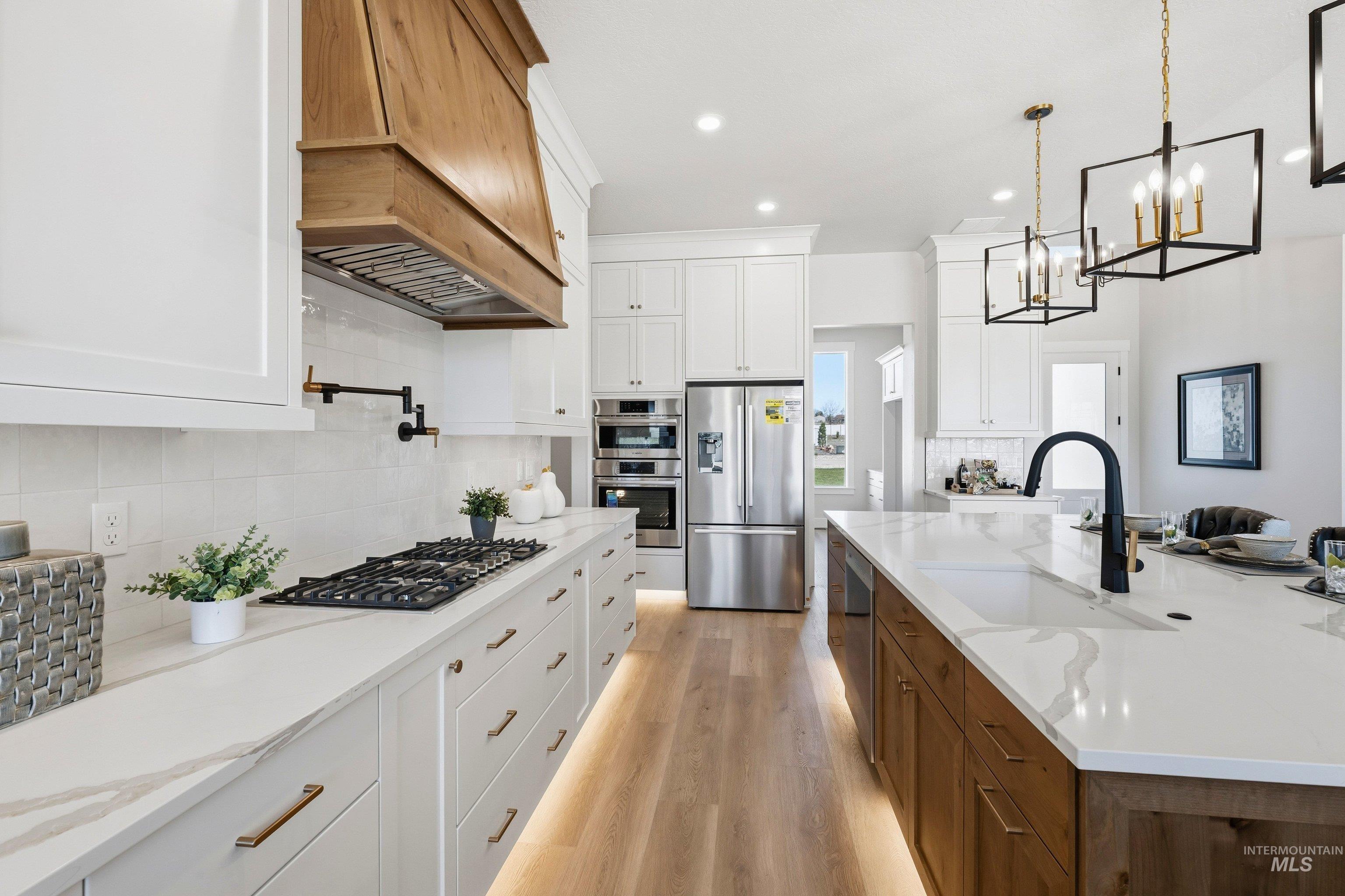 Kitchen with dual tone cabinetry, light stone counters, stainless steel appliances, light wood-style flooring, and a spacious island