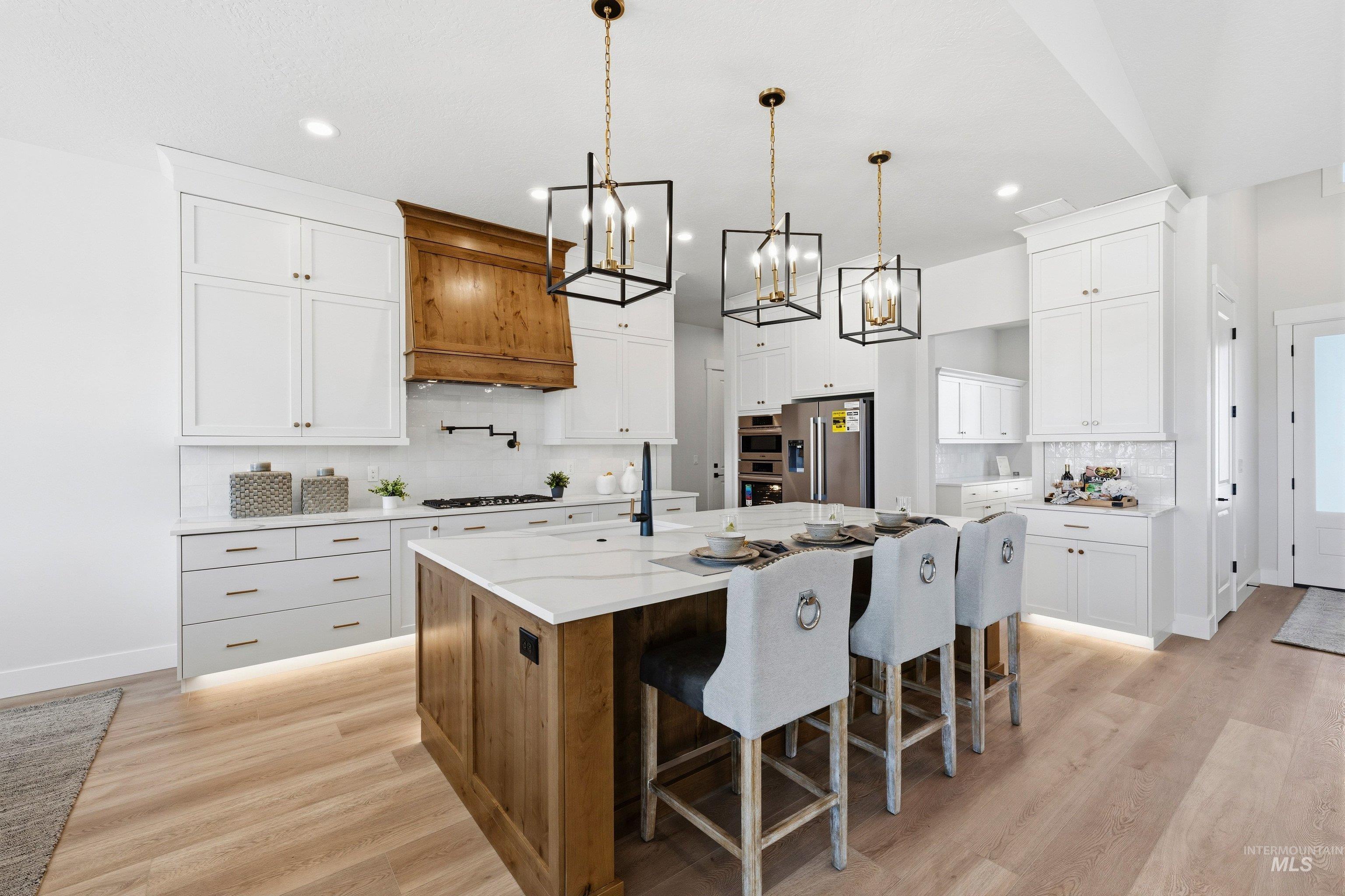 Two tone kitchen featuring two tone cabinetry, a breakfast bar area, a center island with sink, light wood finished floors, and tasteful backsplash