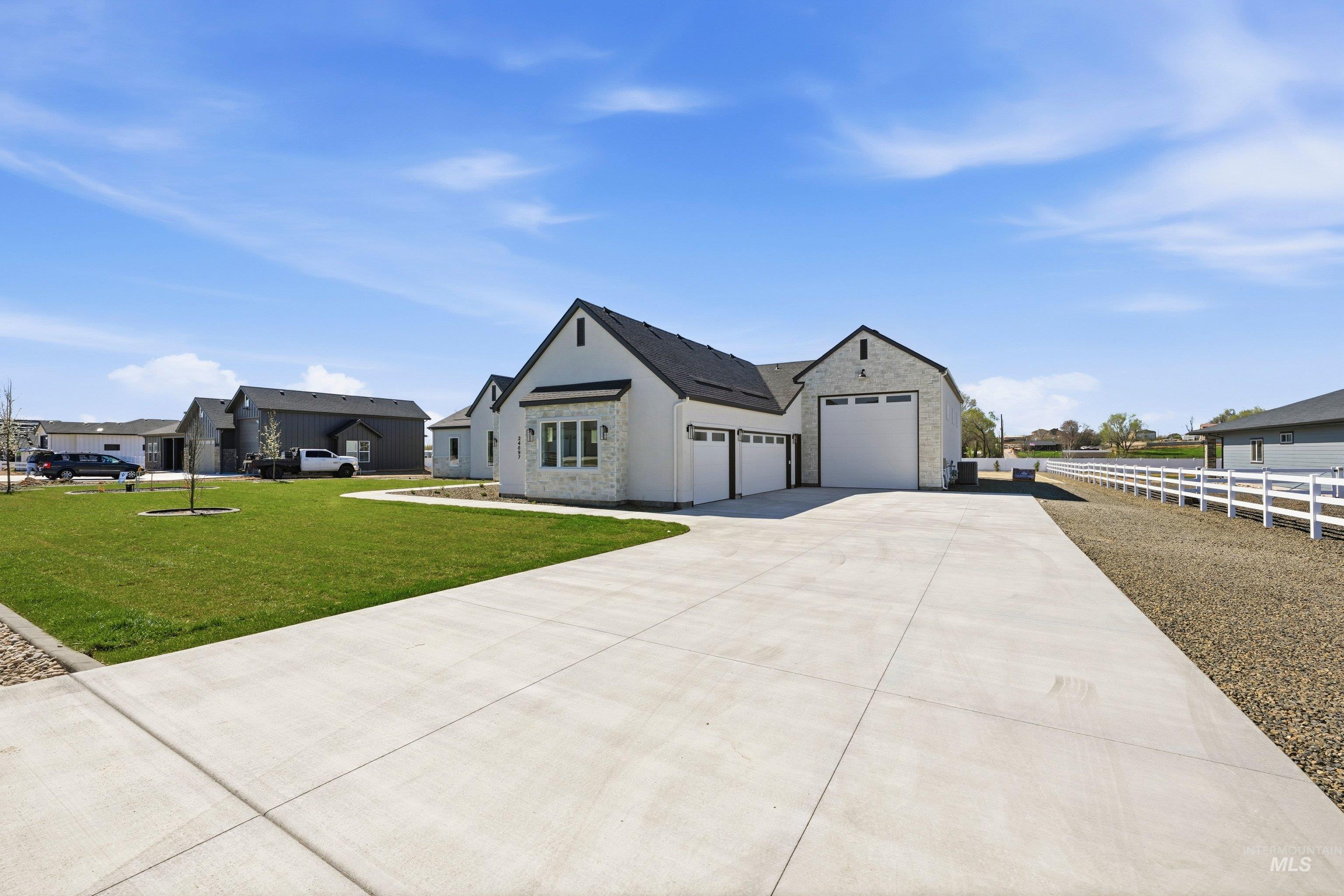 Modern farmhouse with stone siding, concrete driveway, a garage, a residential view, and stucco siding