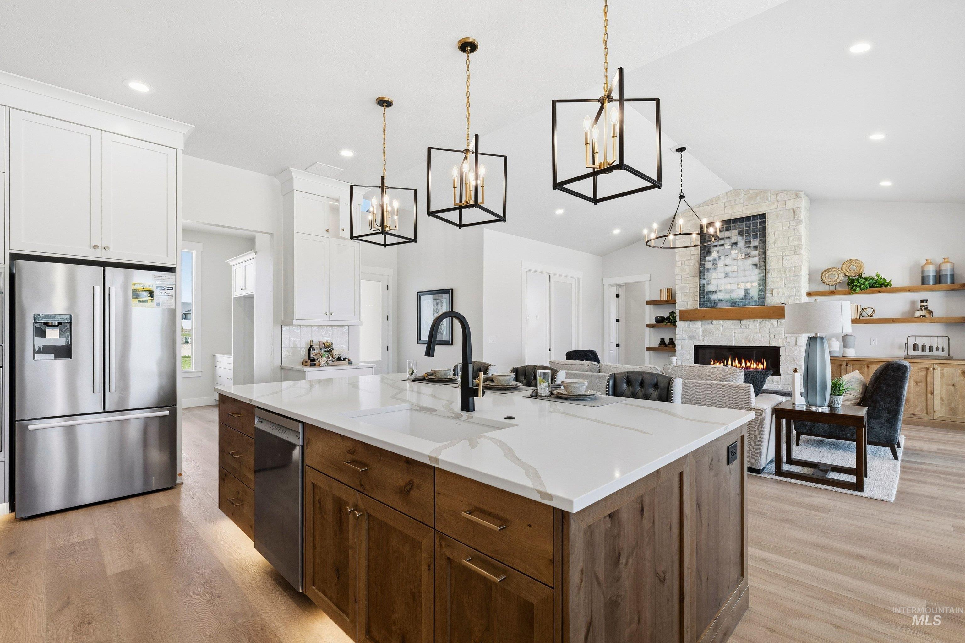 Dual tone kitchen with dual tone cabinets, stainless steel appliances, a stone fireplace, open floor plan, and a center island with sink