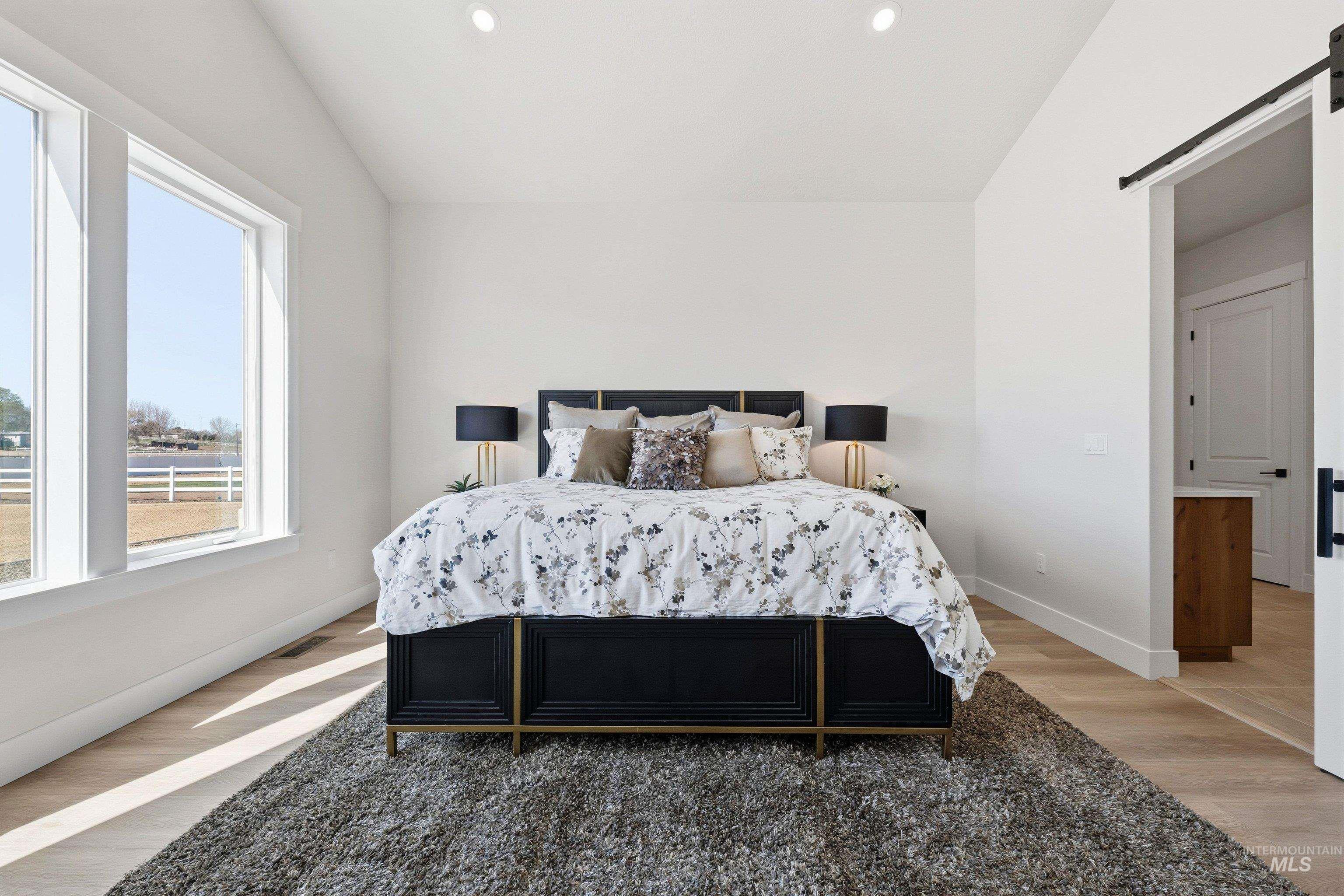 Bedroom featuring a barn door, light wood-style floors, recessed lighting, and lofted ceiling