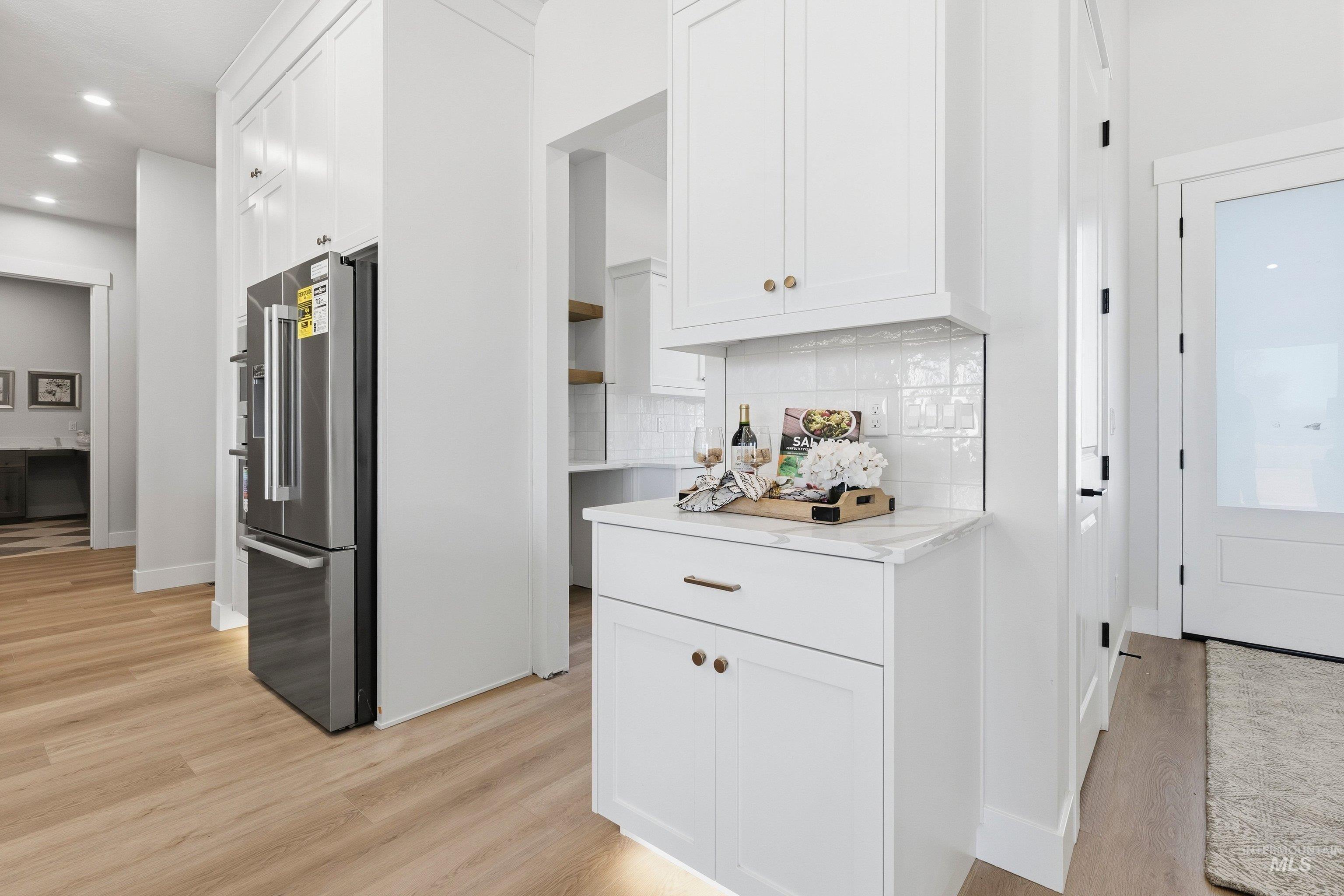 Kitchen with high quality fridge, white cabinets, light wood-style floors, recessed lighting, and tasteful backsplash