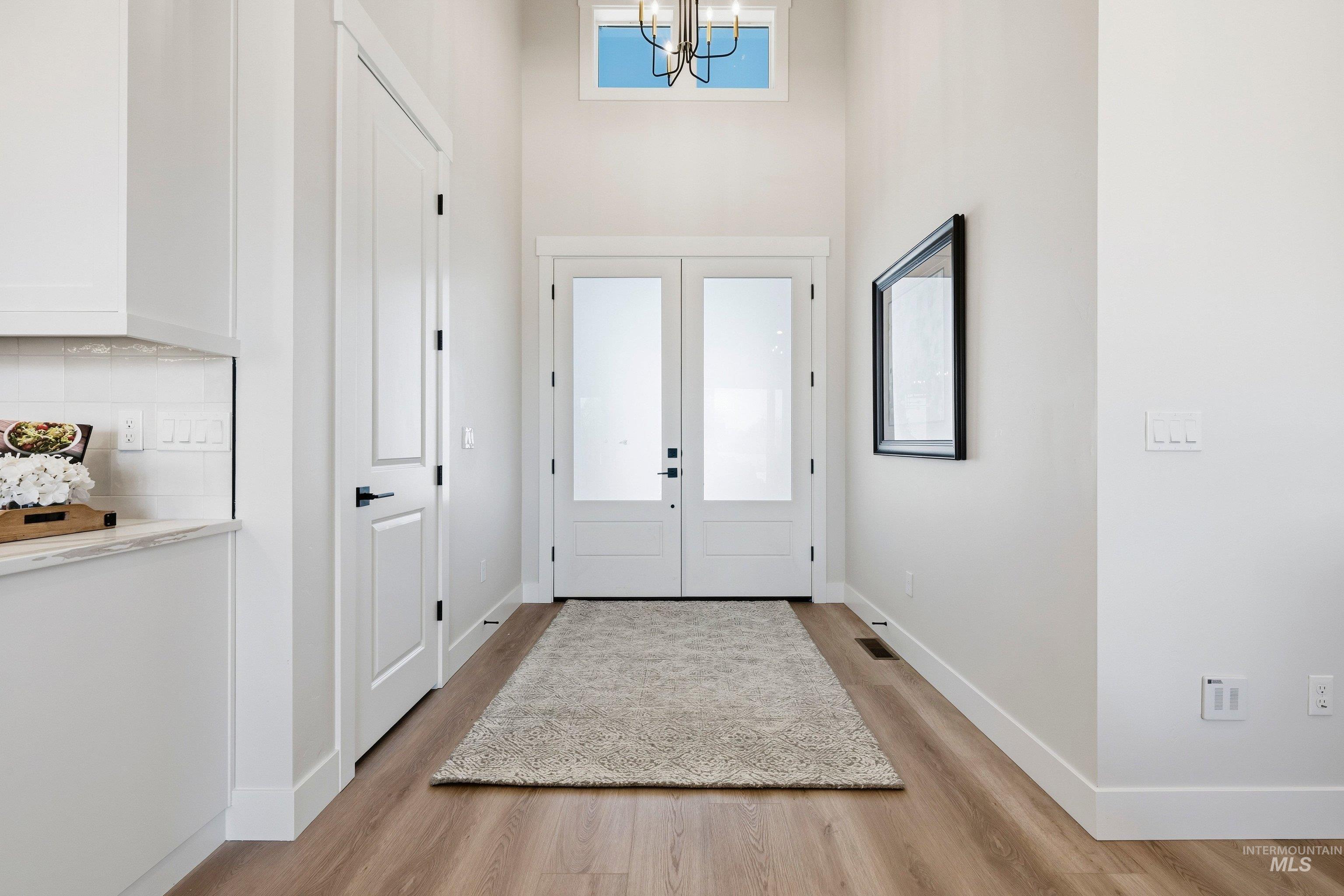 Entryway featuring french doors, a high ceiling, light wood-style flooring, and a chandelier