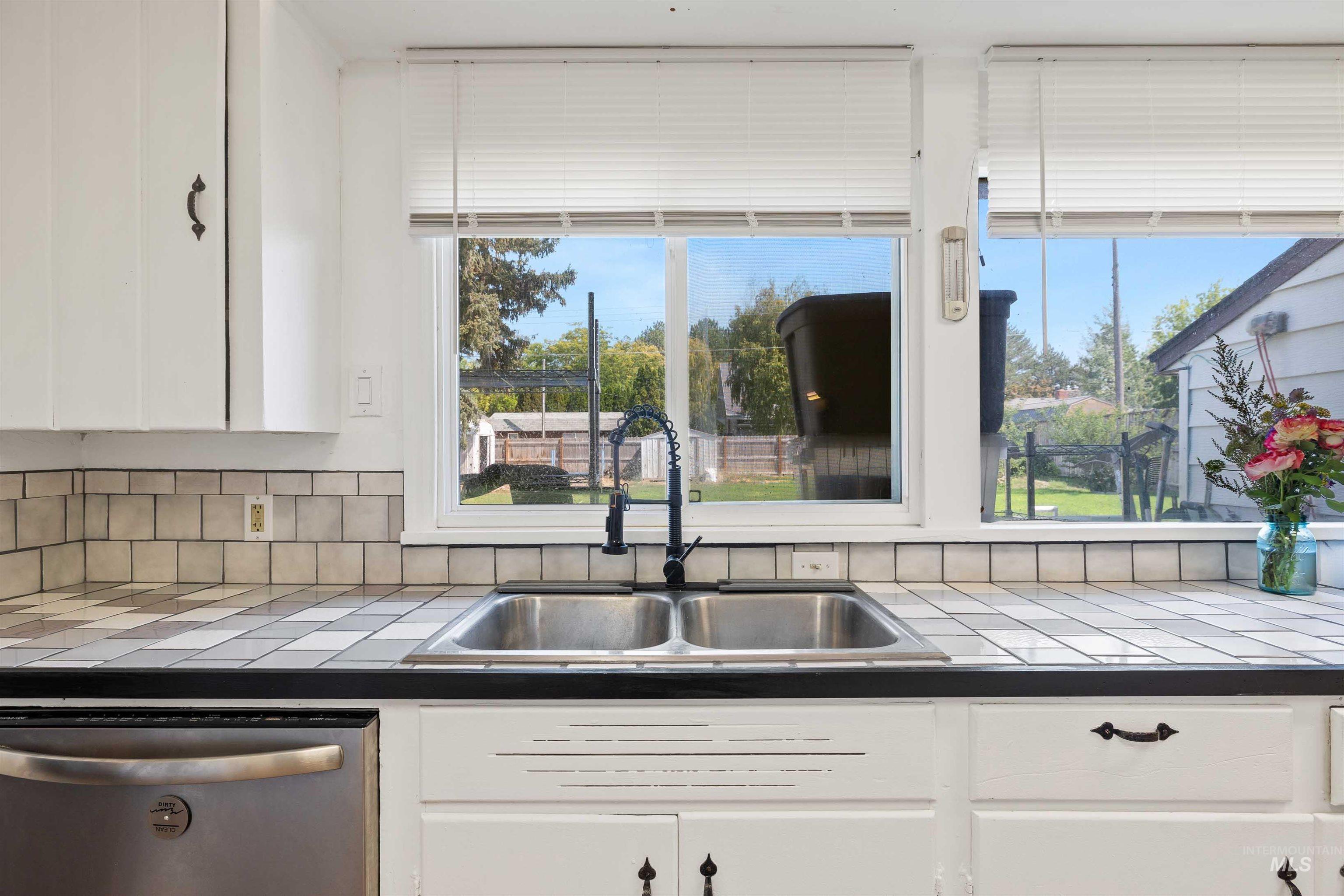 Kitchen with tile counters, white cabinets, dishwasher, and tasteful backsplash