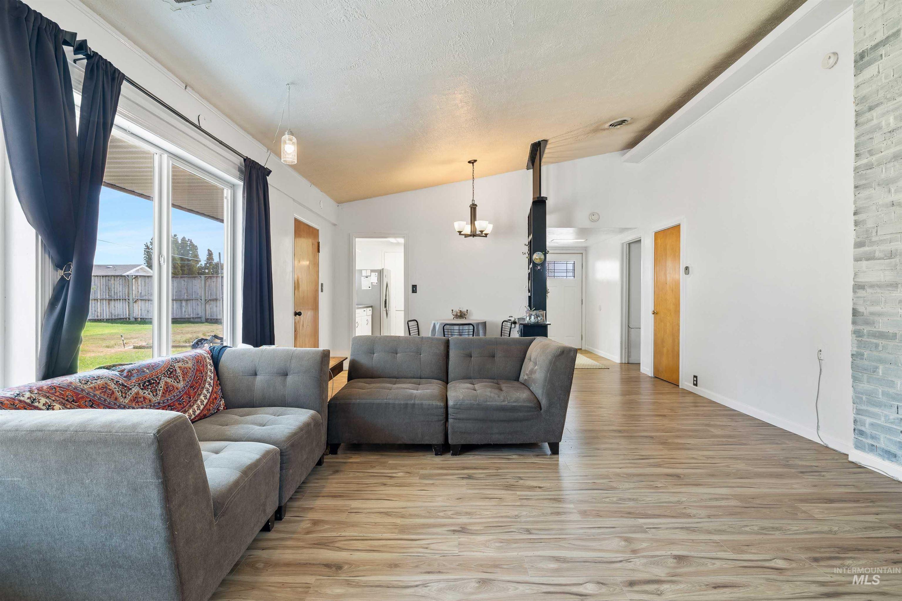 Living area featuring light wood-type flooring, lofted ceiling, a chandelier, and a textured ceiling