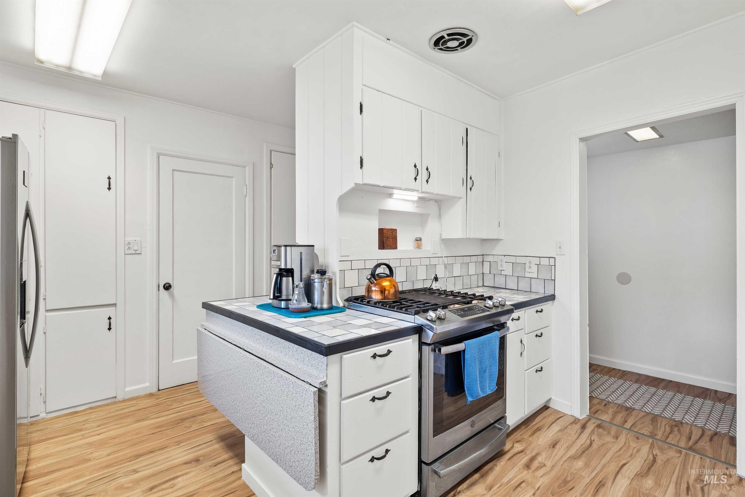 Kitchen with tile countertops, white cabinetry, stainless steel appliances, light wood finished floors, and tasteful backsplash