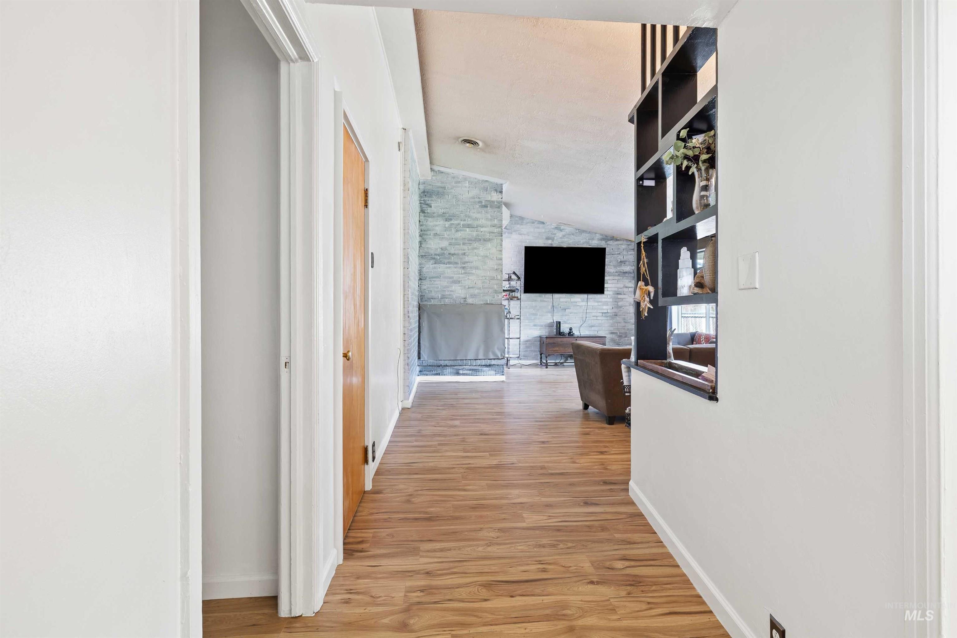 Hallway with light wood-style flooring and vaulted ceiling