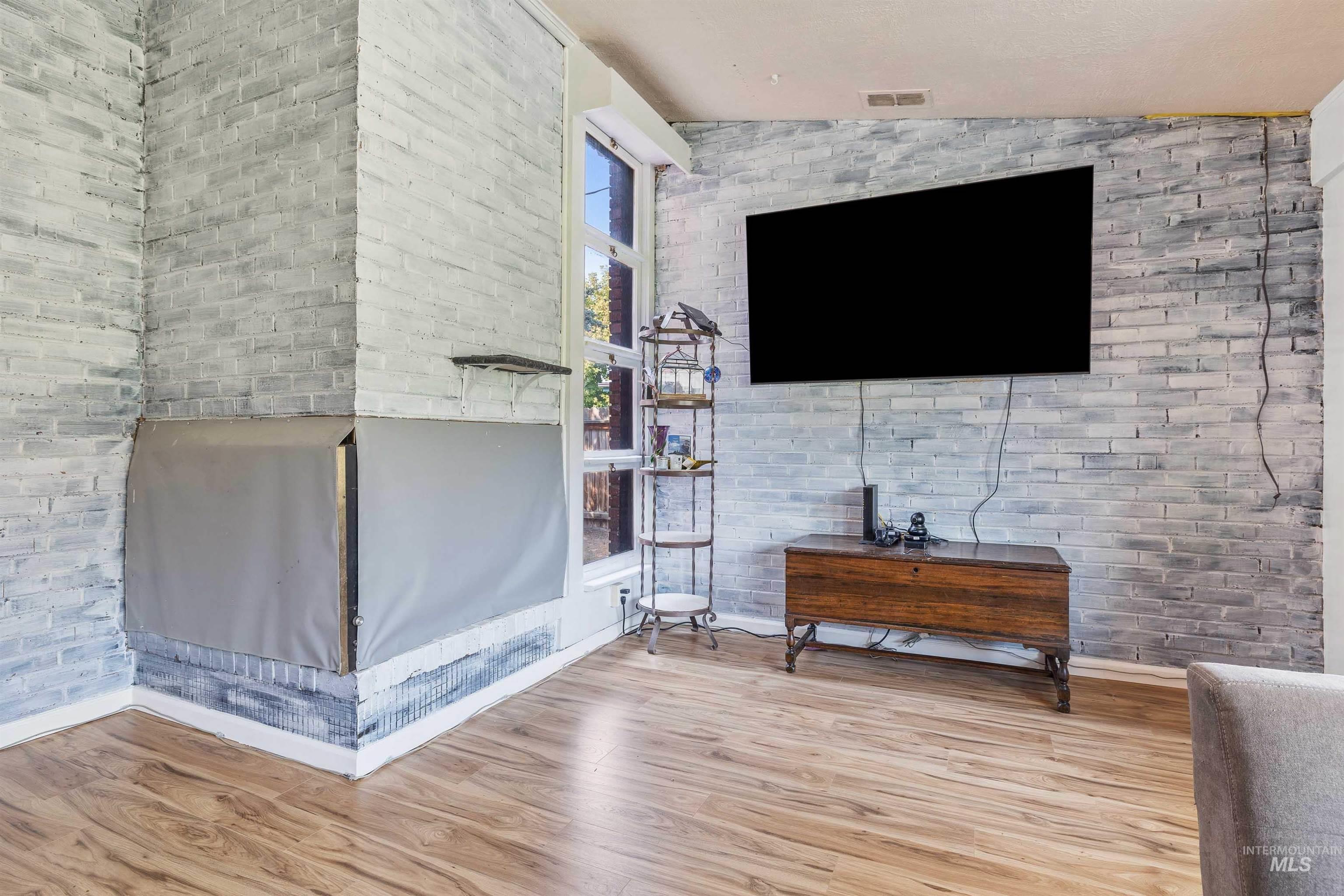 Living area featuring brick wall, light wood finished floors, and vaulted ceiling