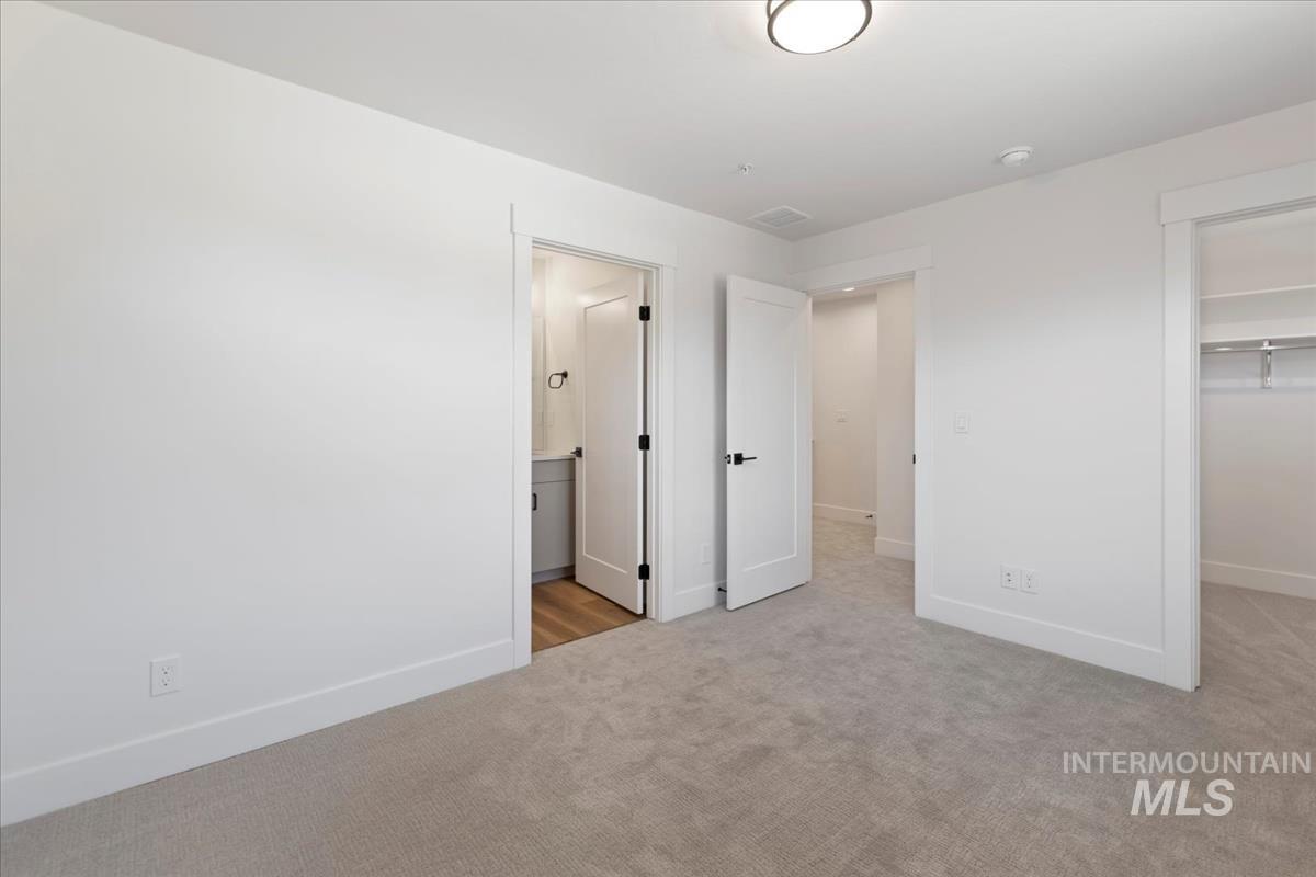 Unfurnished bedroom with a walk in closet, light carpet, and ensuite bathroom