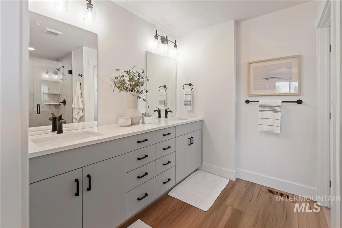 Bathroom with double vanity, light wood-style floors, and a shower stall