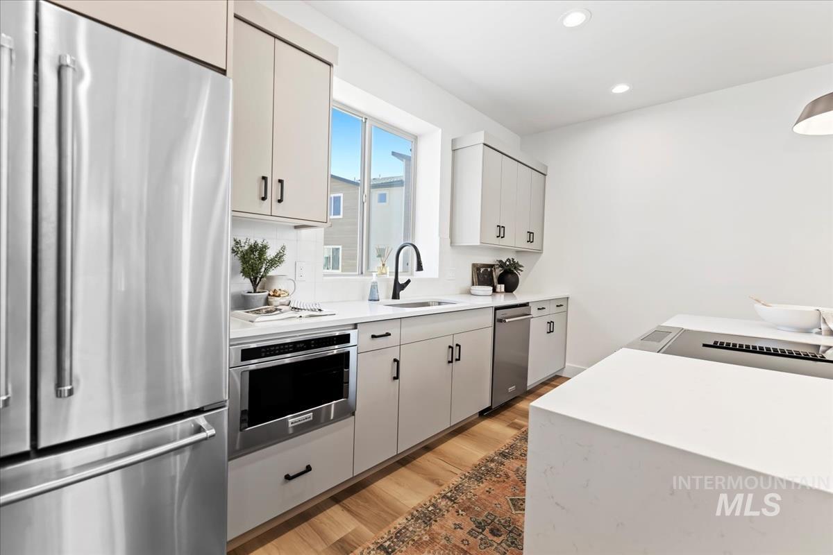 Kitchen with stainless steel appliances, light wood-style floors, recessed lighting, light stone counters, and white cabinets