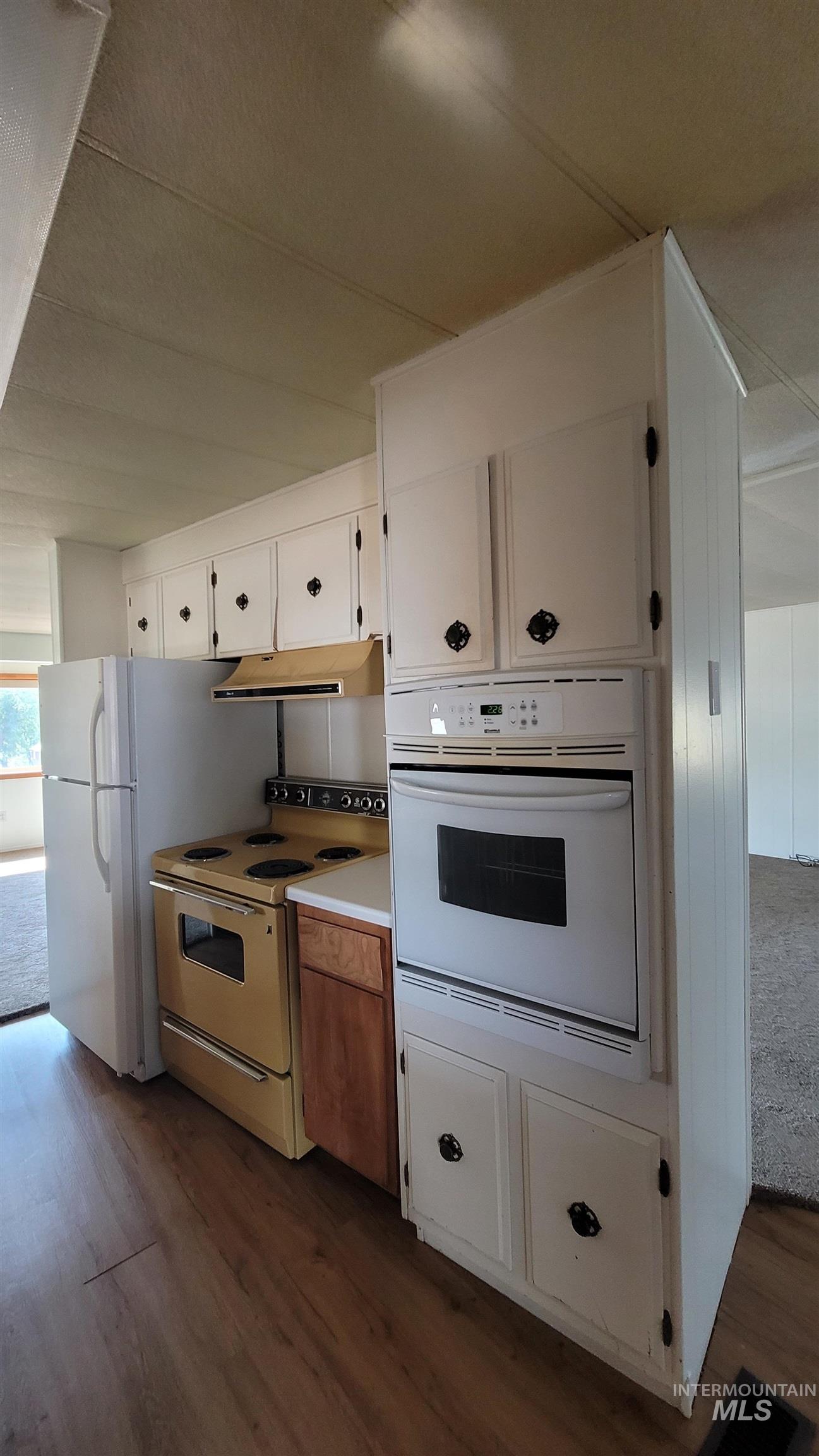 Kitchen featuring white appliances, white cabinetry, dark wood-style floors, light countertops, and under cabinet range hood