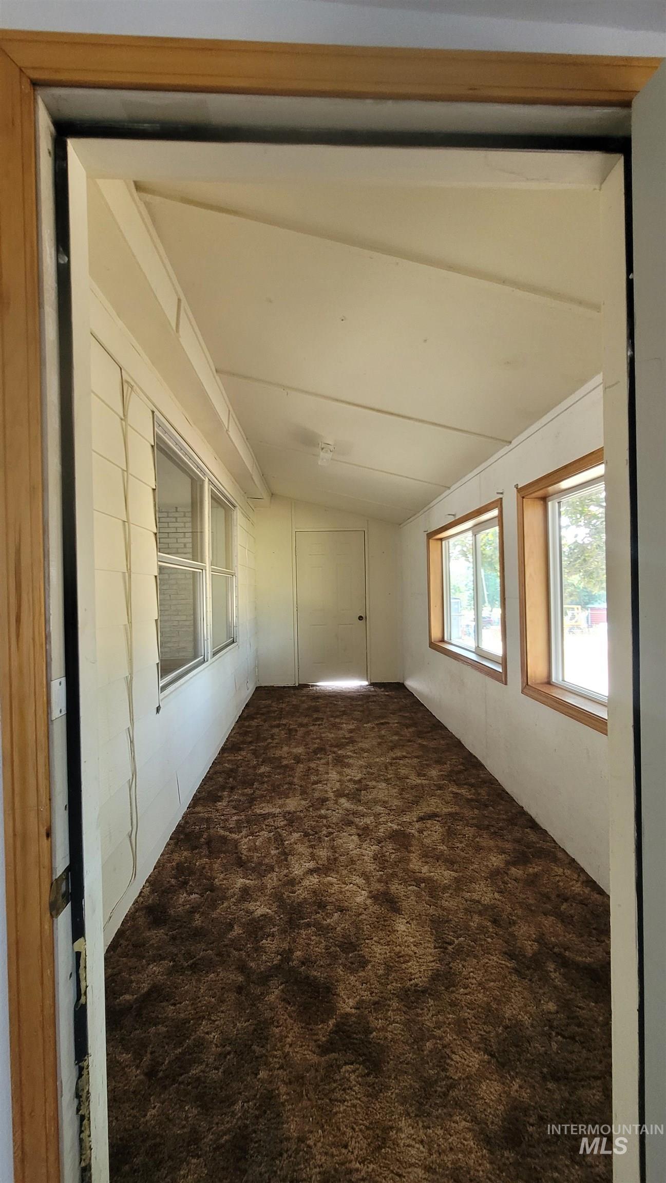 Unfurnished room with dark colored carpet and lofted ceiling