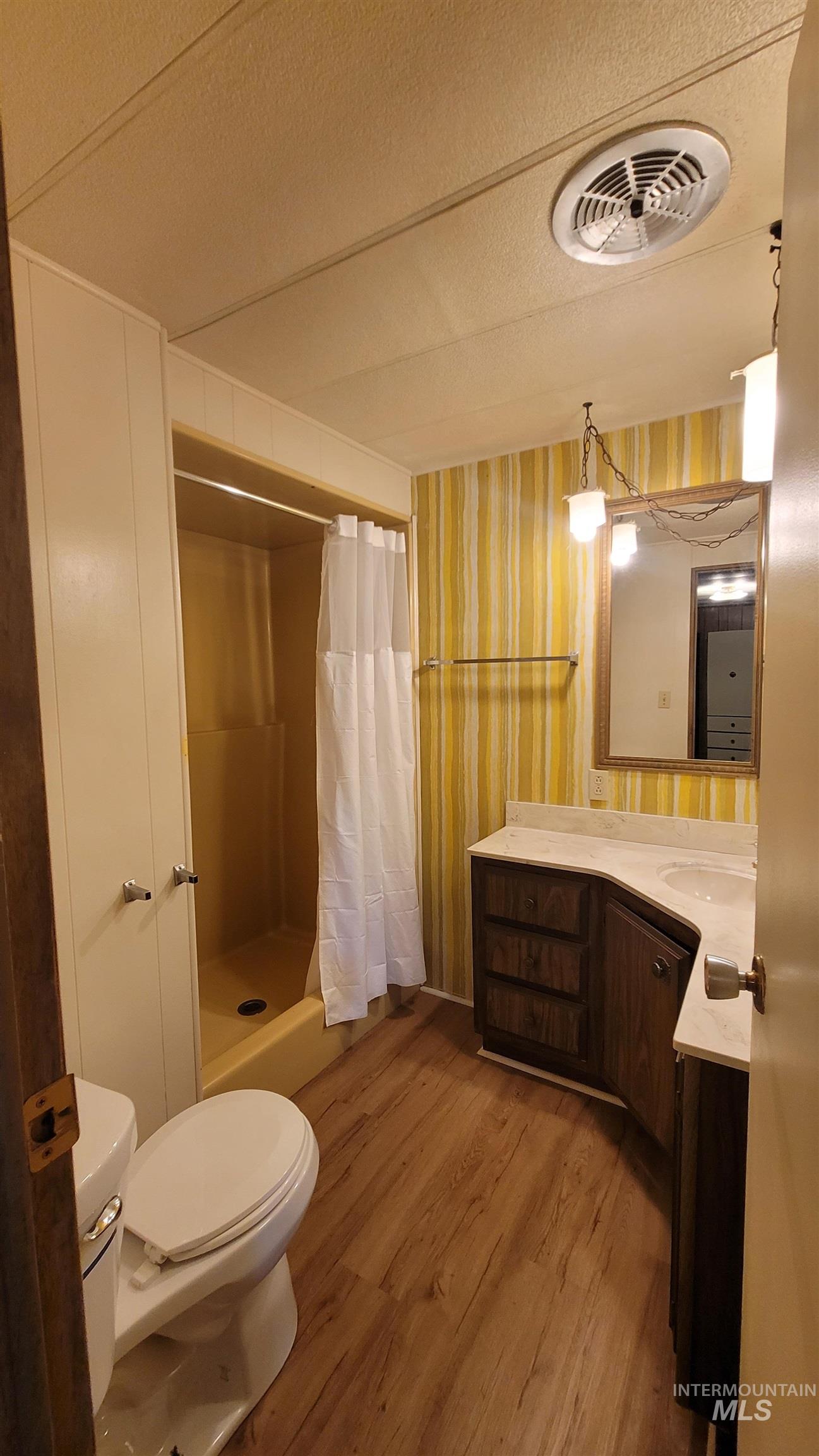 Full bathroom with vanity, a shower stall, light wood-style flooring, and a textured ceiling