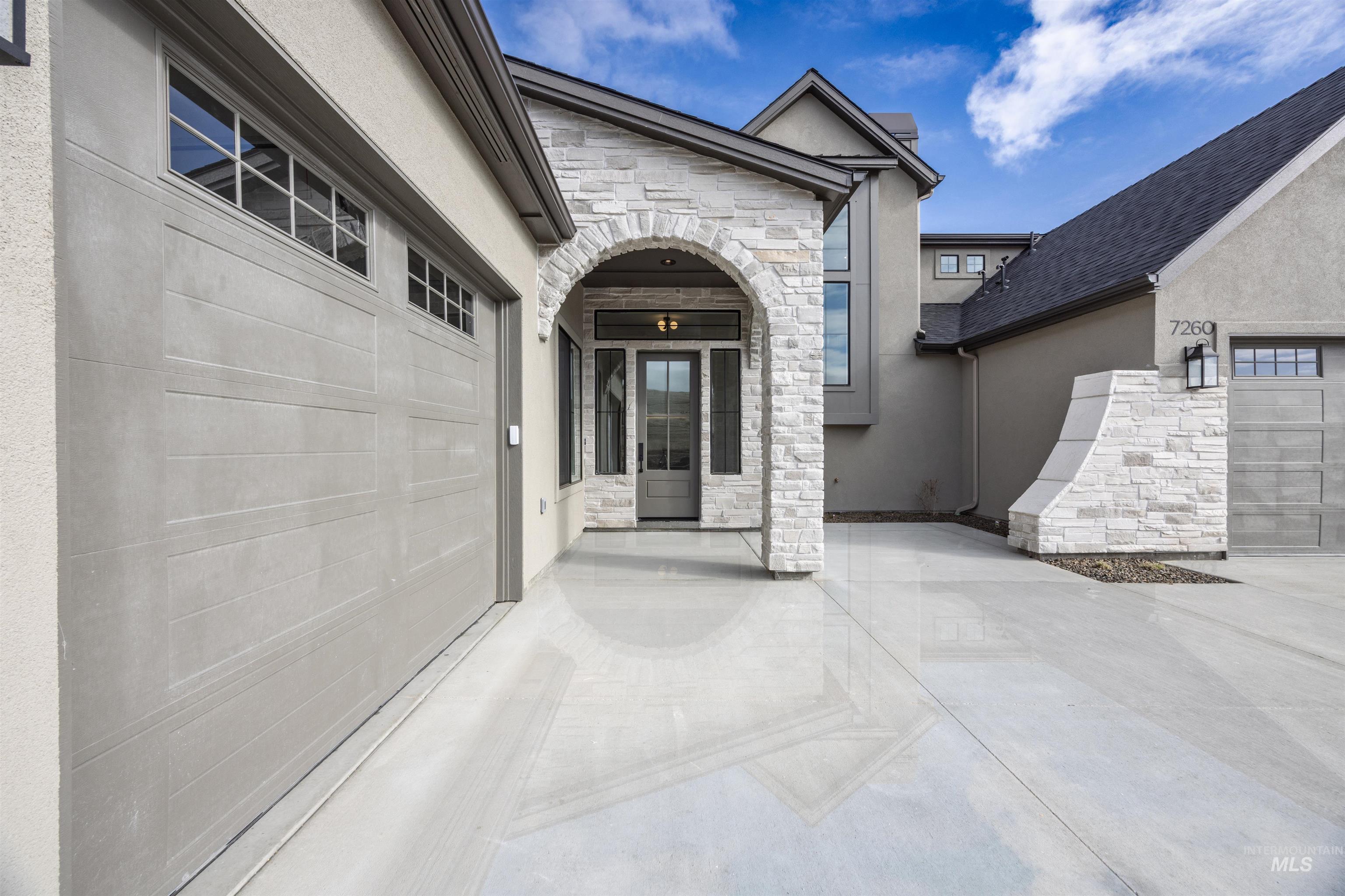 Doorway to property with stone siding, stucco siding, an attached garage, and concrete driveway