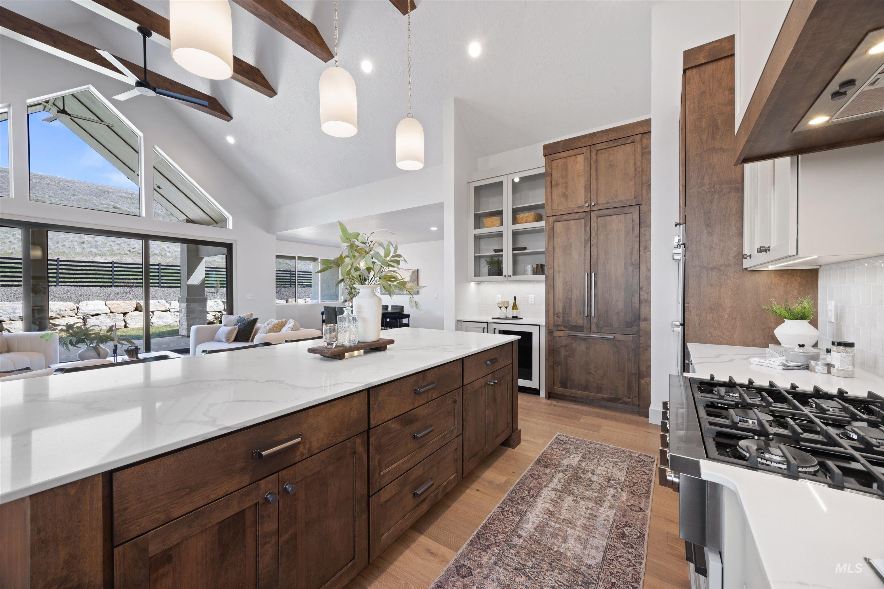 Dual tone kitchen featuring light stone counters, range hood, gas range oven, decorative light fixtures, and two tone color scheme