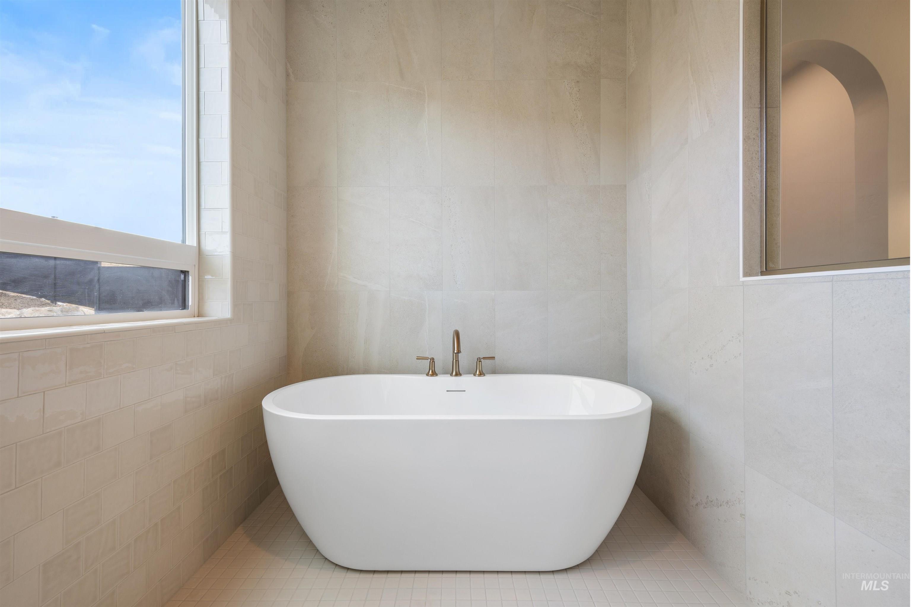 Full bathroom featuring tile walls, a freestanding bath, and tile patterned floors