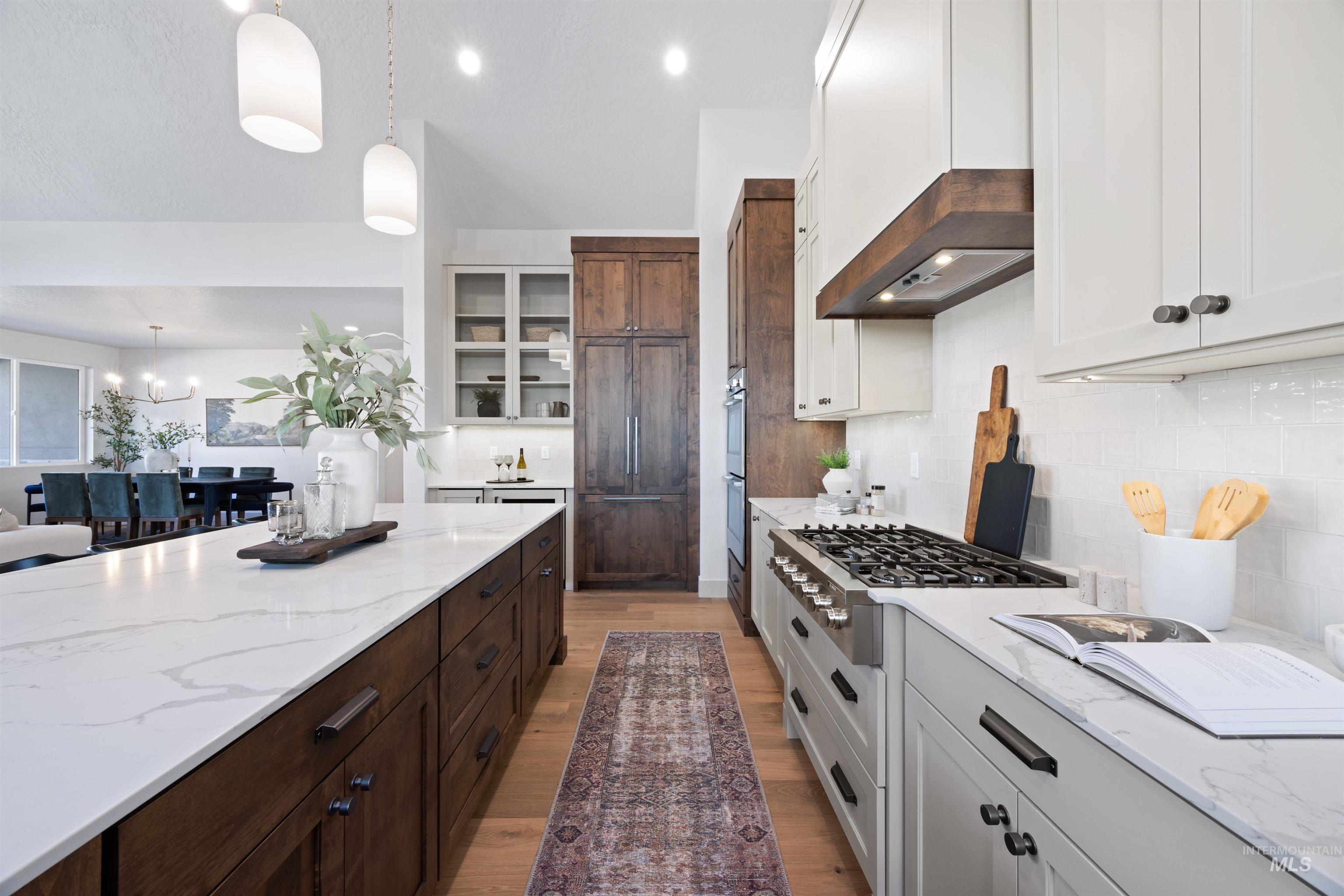 Kitchen with light stone countertops, dual tone cabinets, stainless steel gas cooktop, decorative backsplash, and light wood-style floors