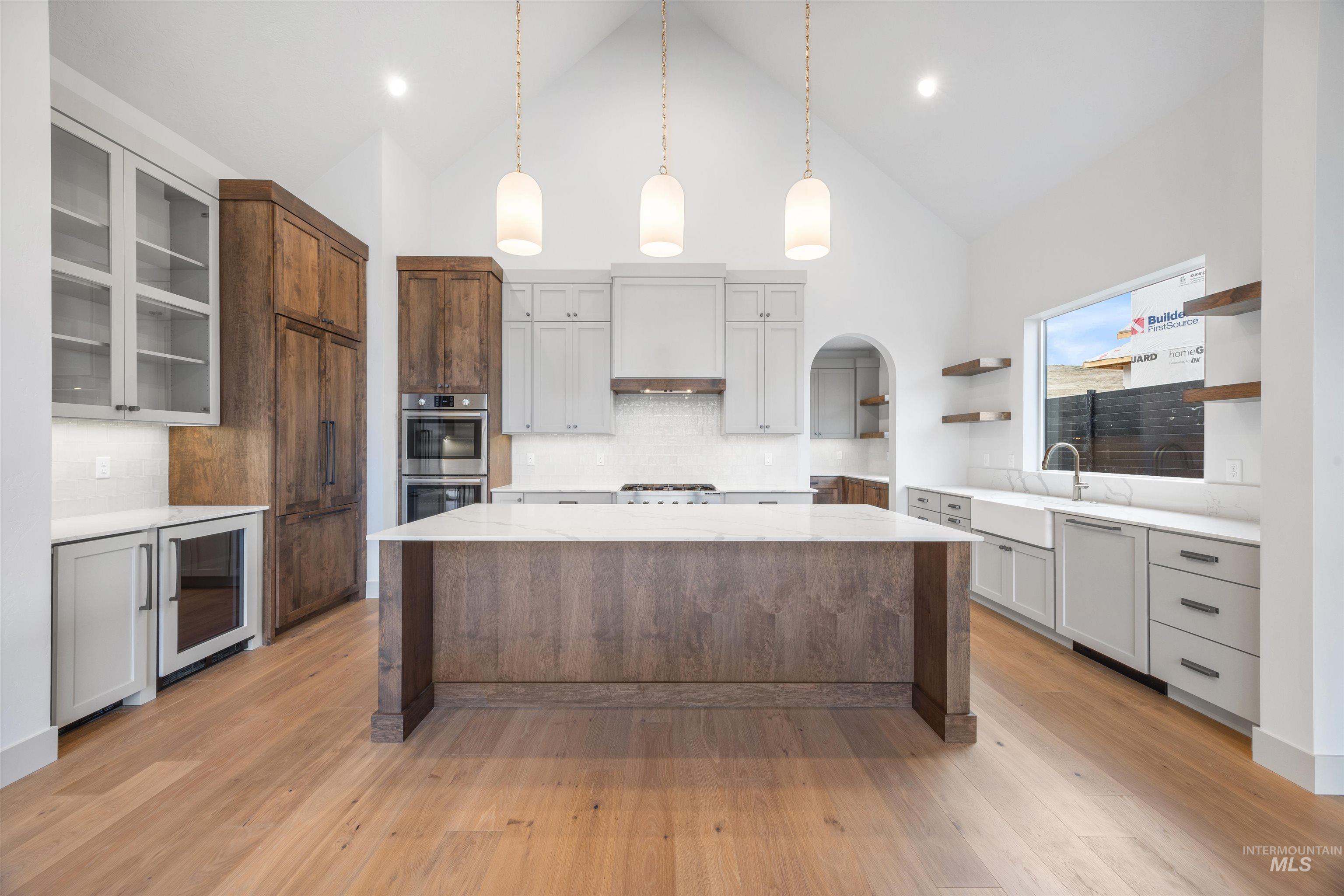 Kitchen with open shelves, pendant lighting, light stone counters, a center island, and wine cooler