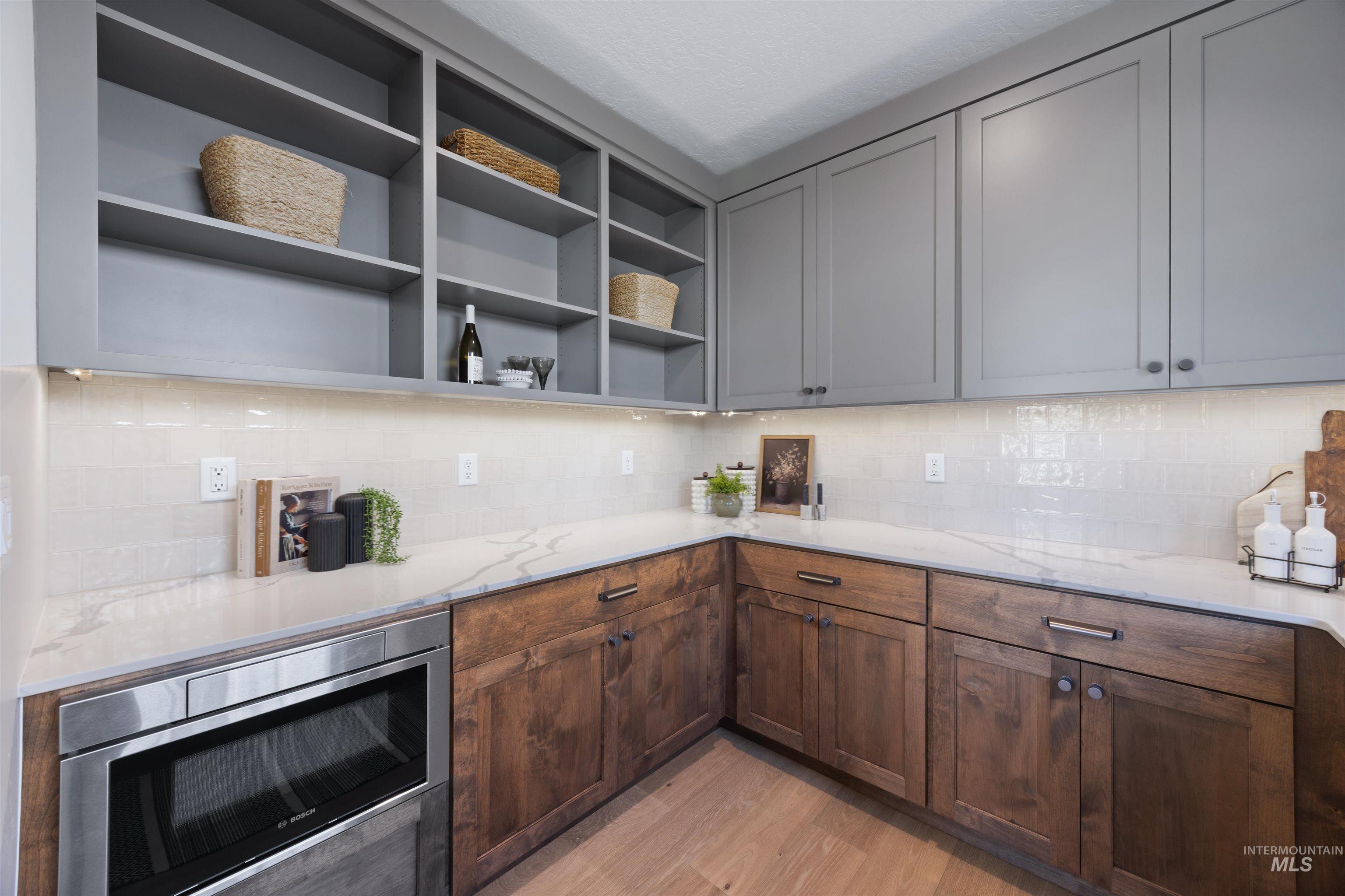 Kitchen with stainless steel microwave, backsplash, light wood-style flooring, light stone counters, and open shelves