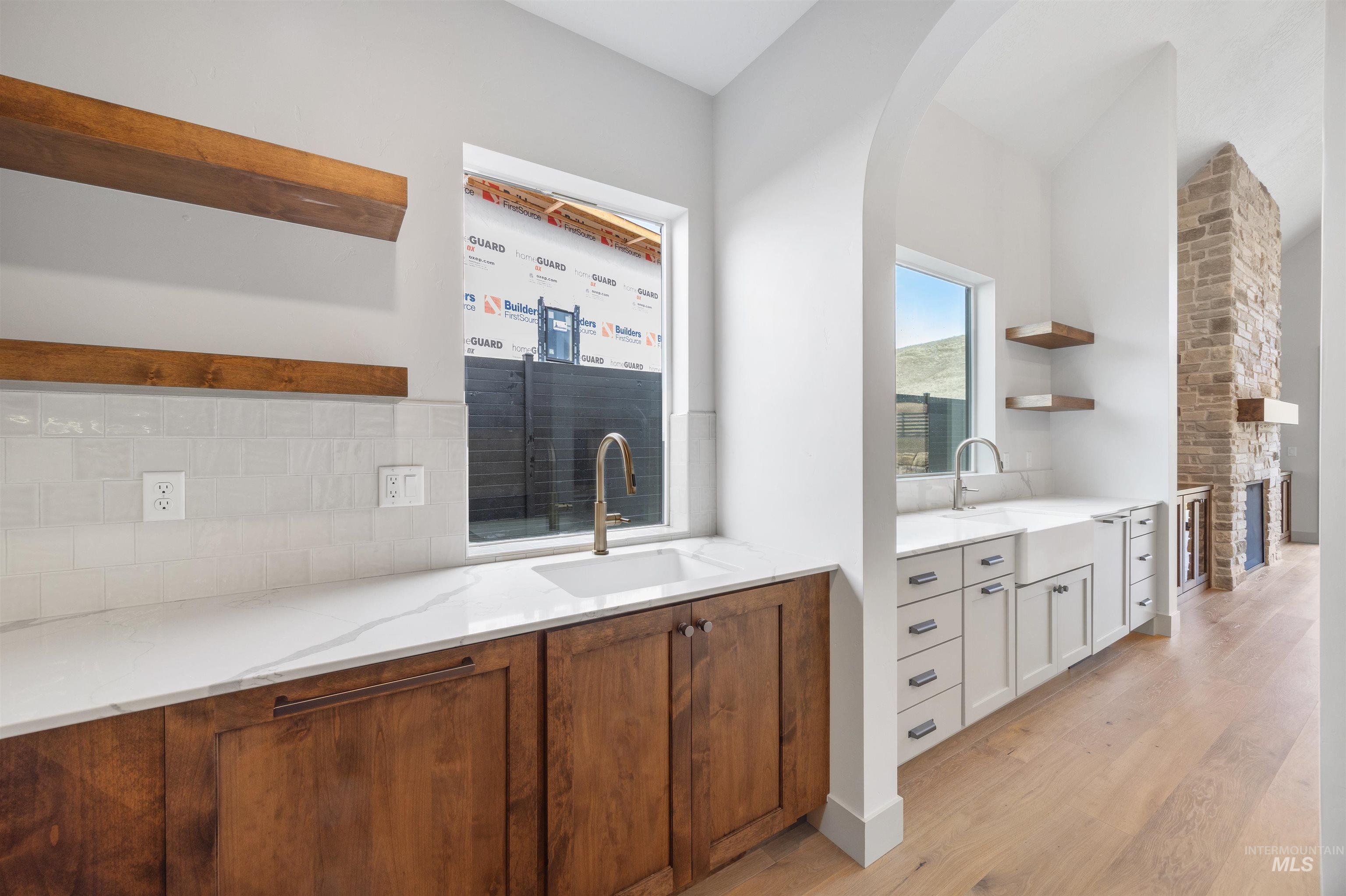 Bar featuring open shelves, light stone counters, light wood-style flooring, wood finish cabinetry, and decorative backsplash