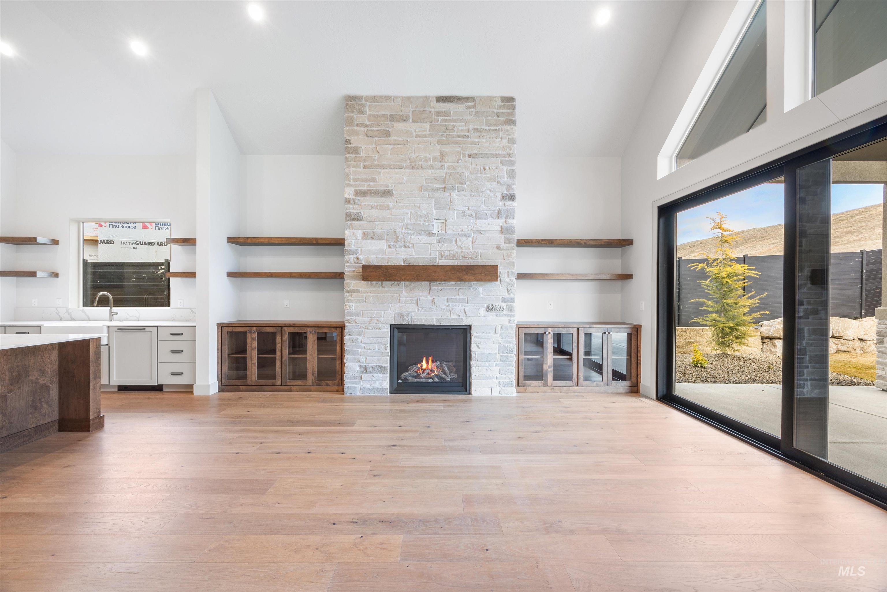 Unfurnished living room with lofted ceiling, light wood-style floors, a stone fireplace, and recessed lighting