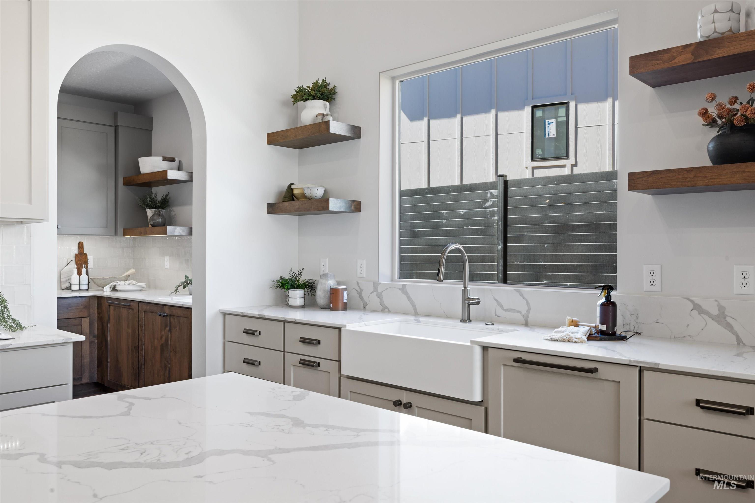 Kitchen featuring open shelves, light stone counters, and backsplash