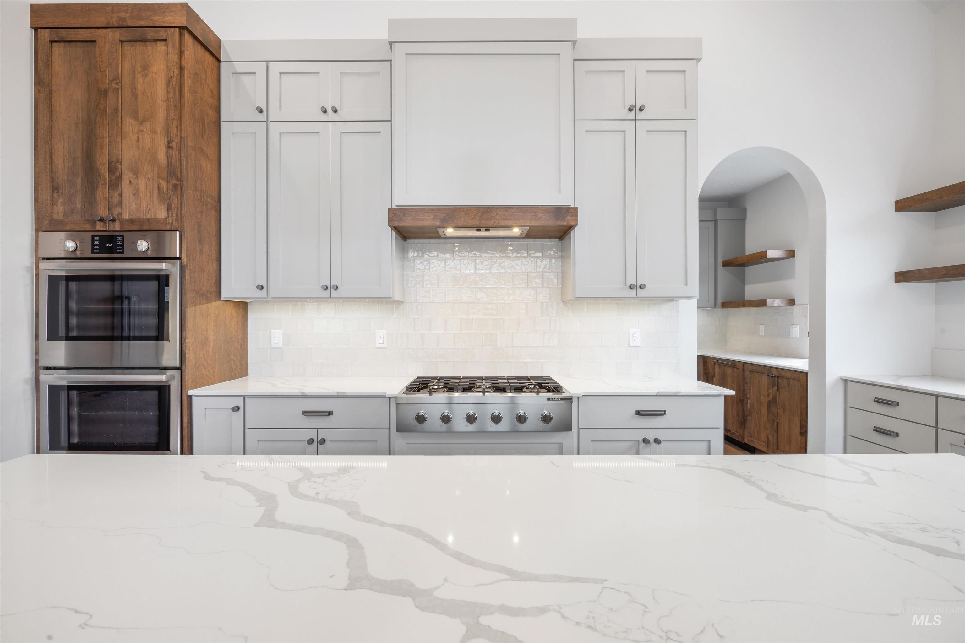 Kitchen with light stone counters, stainless steel appliances, open shelves, and backsplash