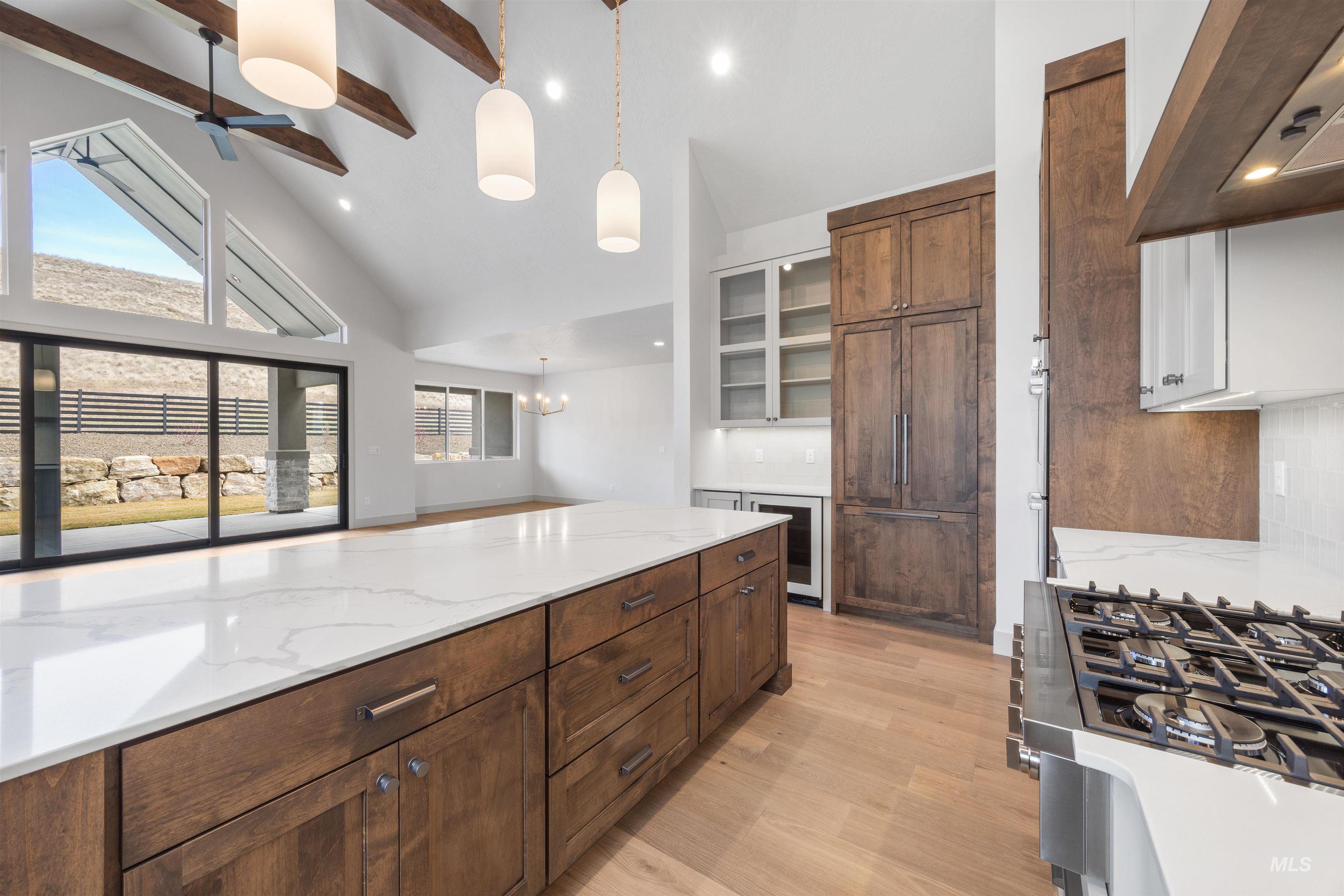 Kitchen featuring two tone cabinetry, range hood, light stone countertops, beverage cooler, and light wood-style flooring