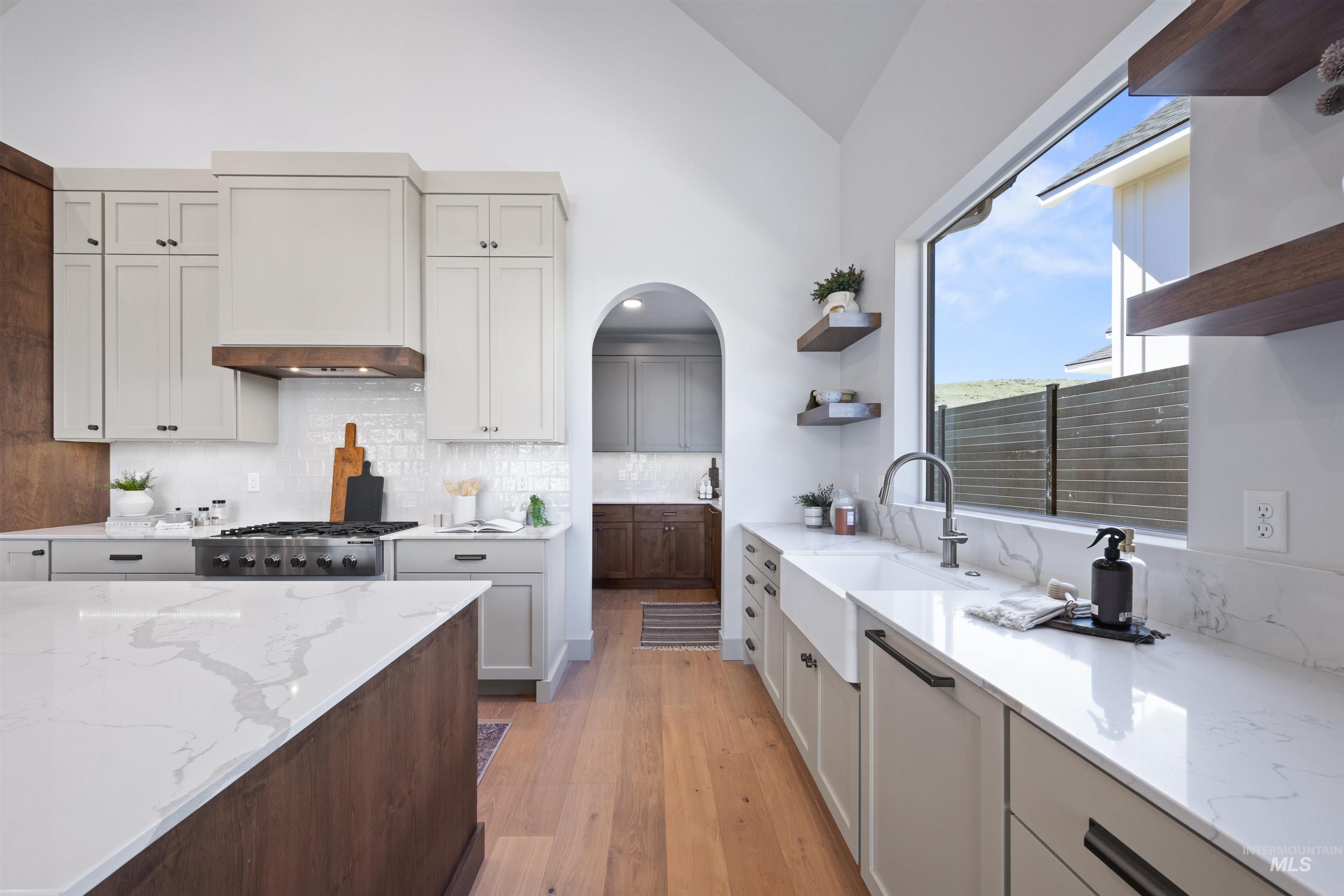 Two tone kitchen with open shelves, light stone countertops, lofted ceiling, dual tone cabinets, and light wood-type flooring