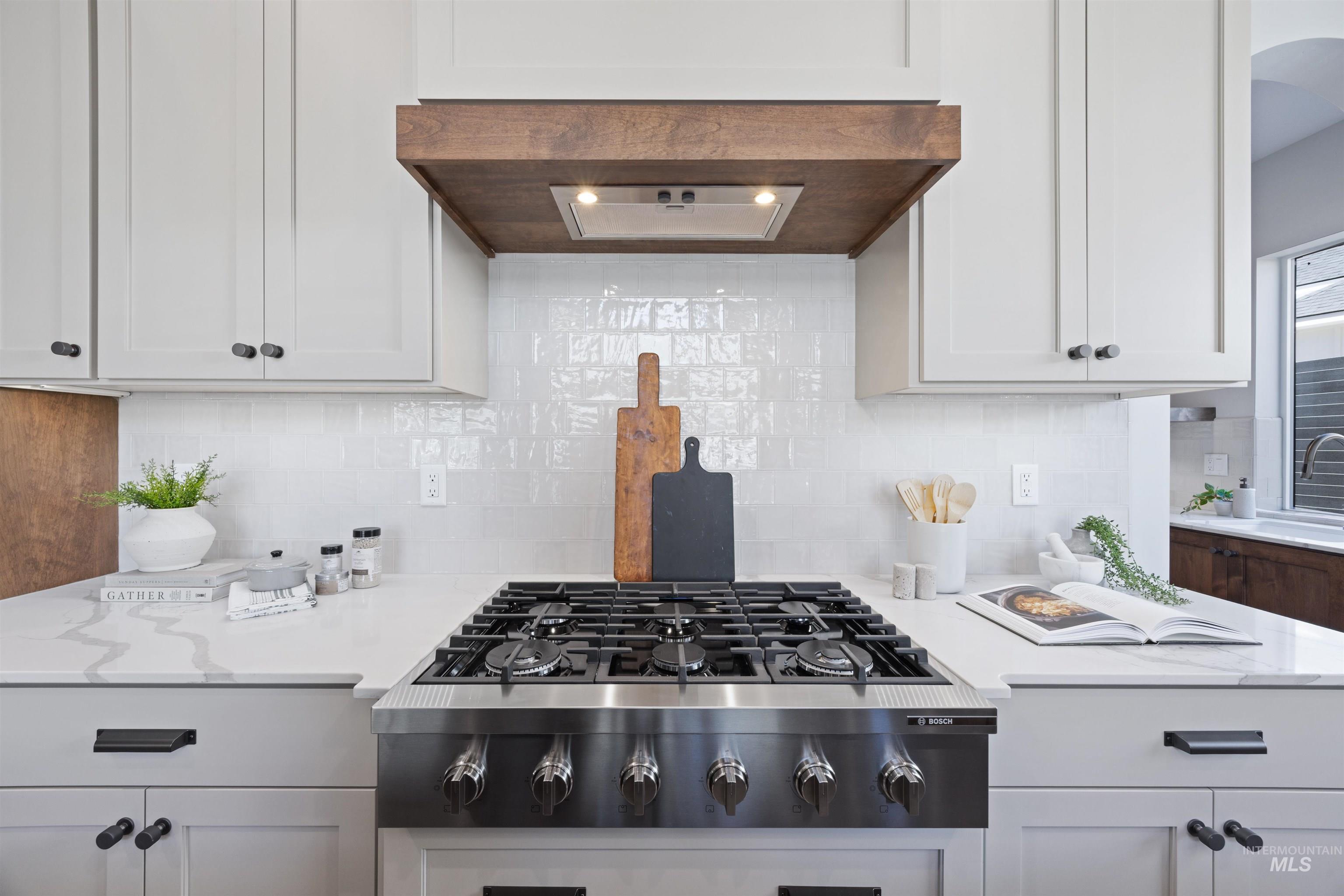 Kitchen featuring stainless steel gas cooktop, white cabinets, light stone countertops, exhaust hood, and tasteful backsplash