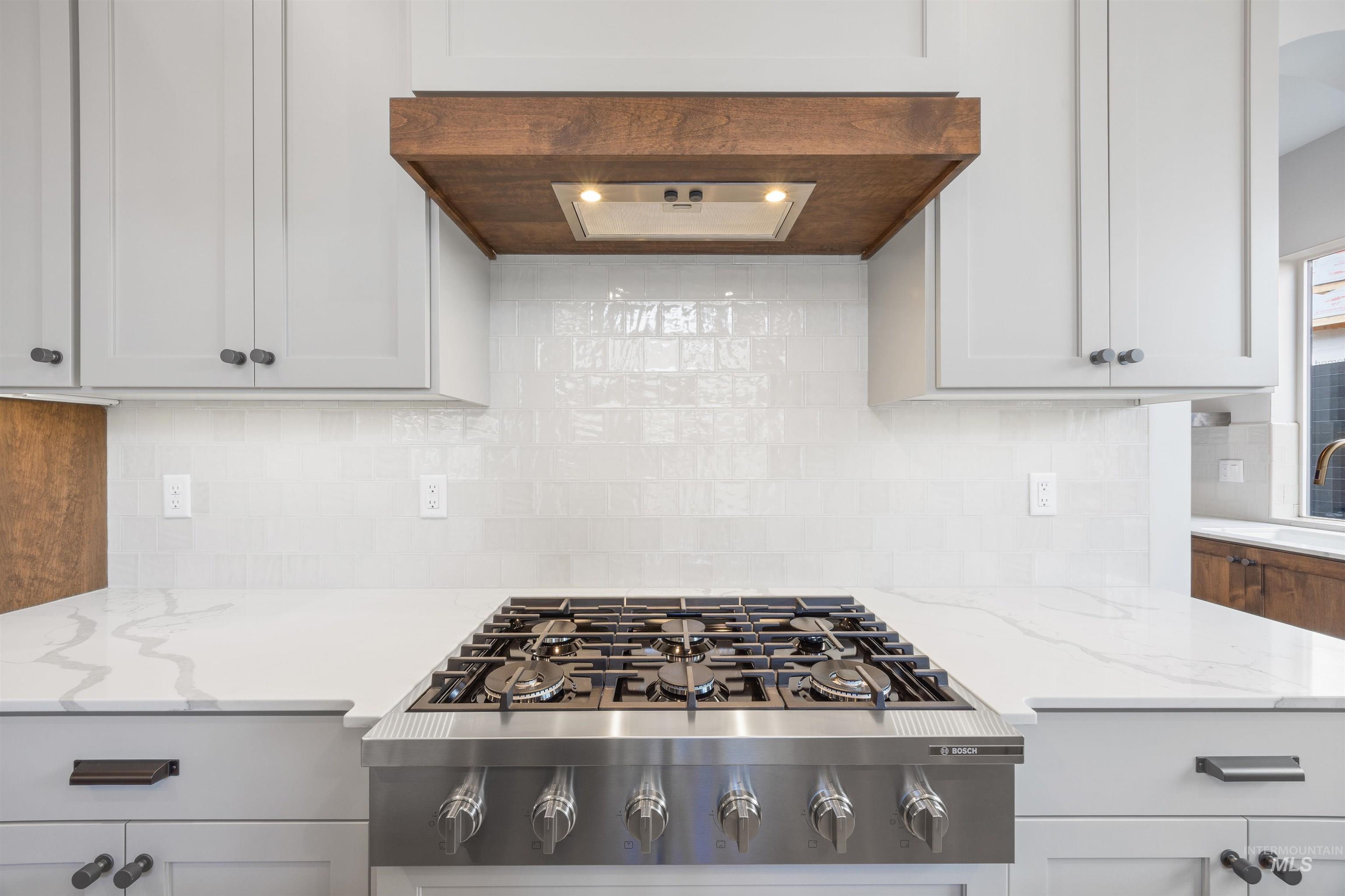 Kitchen featuring white cabinets, stainless steel gas cooktop, light stone countertops, and extractor fan