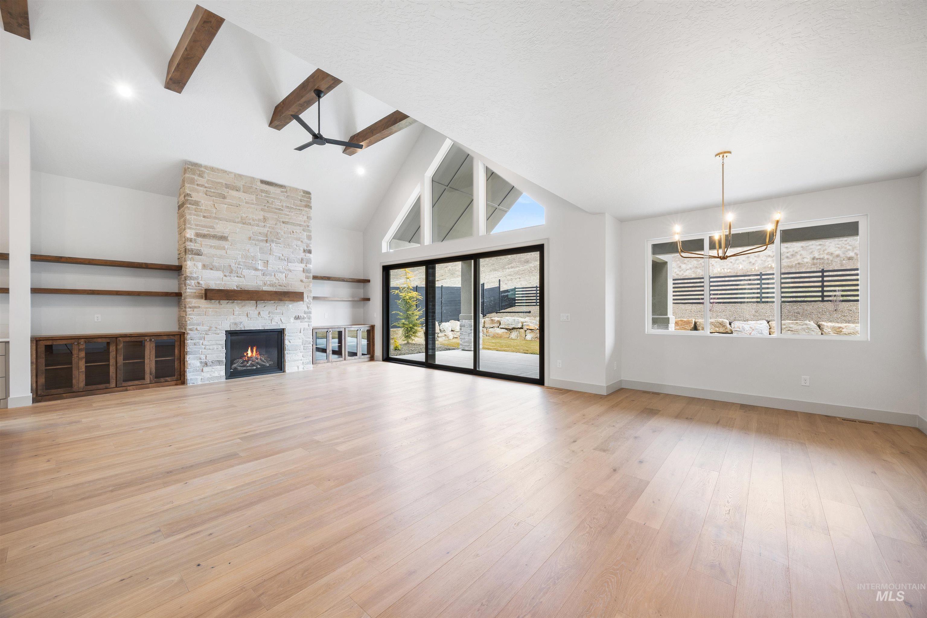 Unfurnished living room featuring a fireplace, light wood-style floors, vaulted ceiling, and suspended lighting