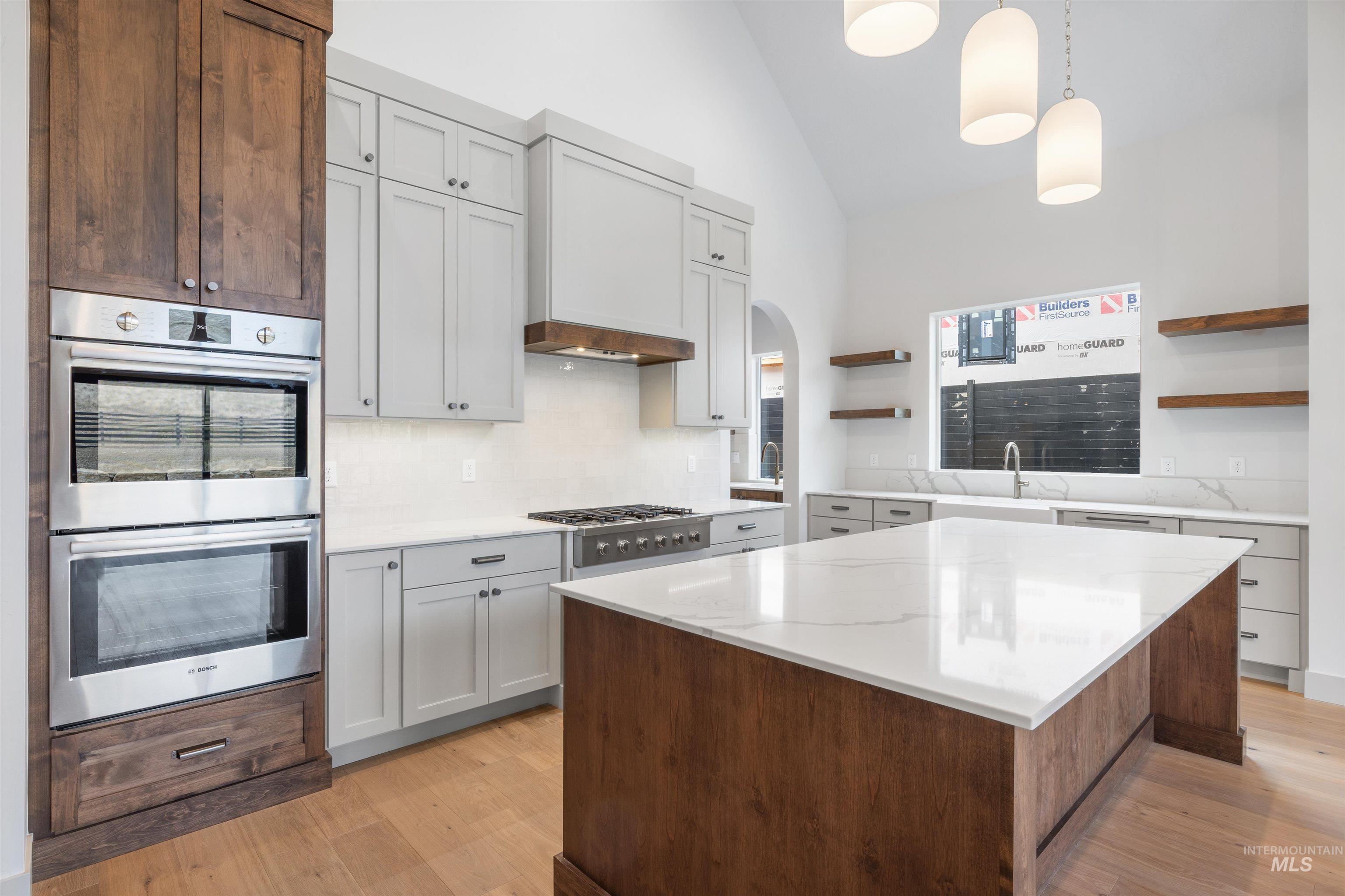 Kitchen featuring open shelves, stainless steel appliances, lofted ceiling, arched walkways, and light wood-style flooring
