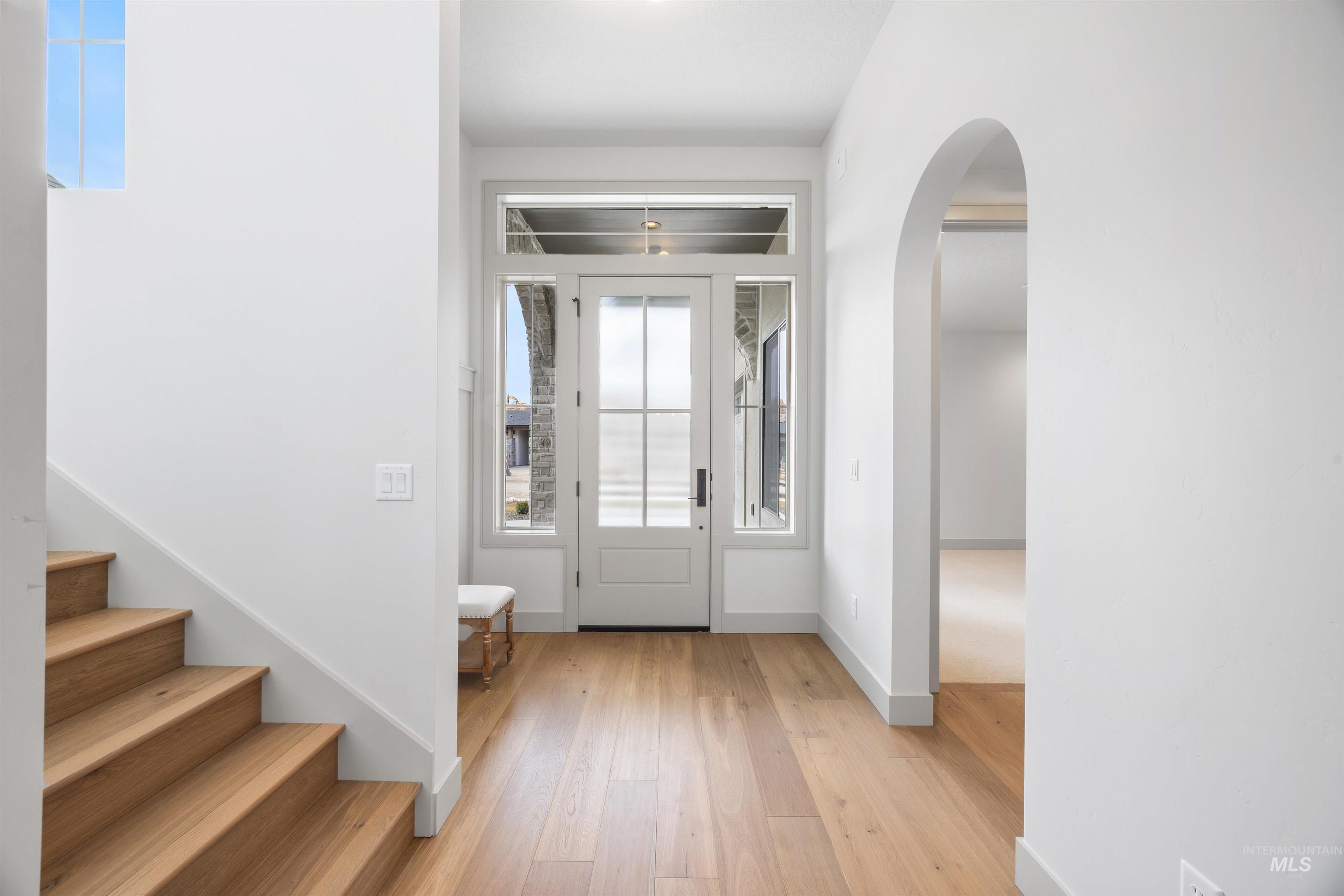 Foyer with arched walkways and light wood-type flooring