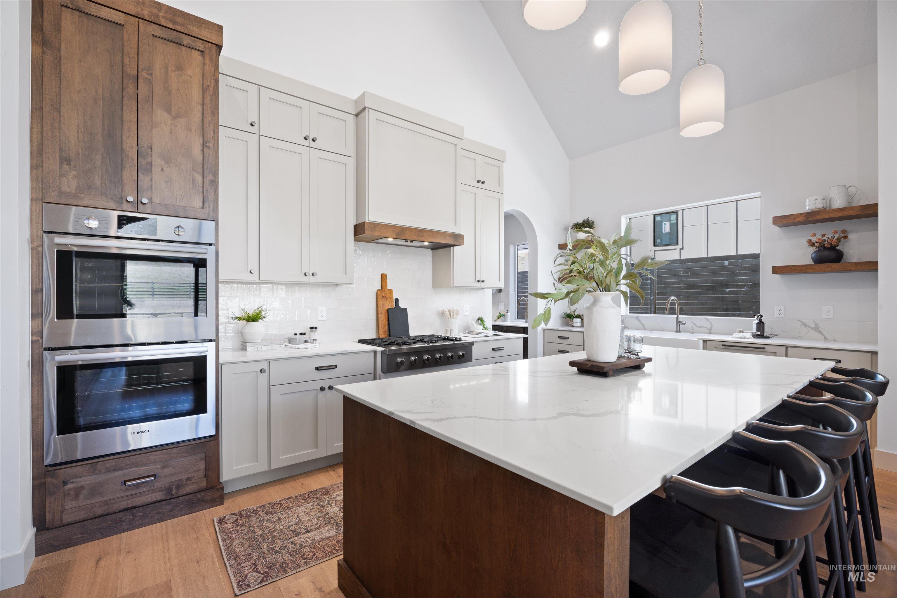 Kitchen featuring vaulted ceiling, arched walkways, stainless steel appliances, light stone countertops, and tasteful backsplash