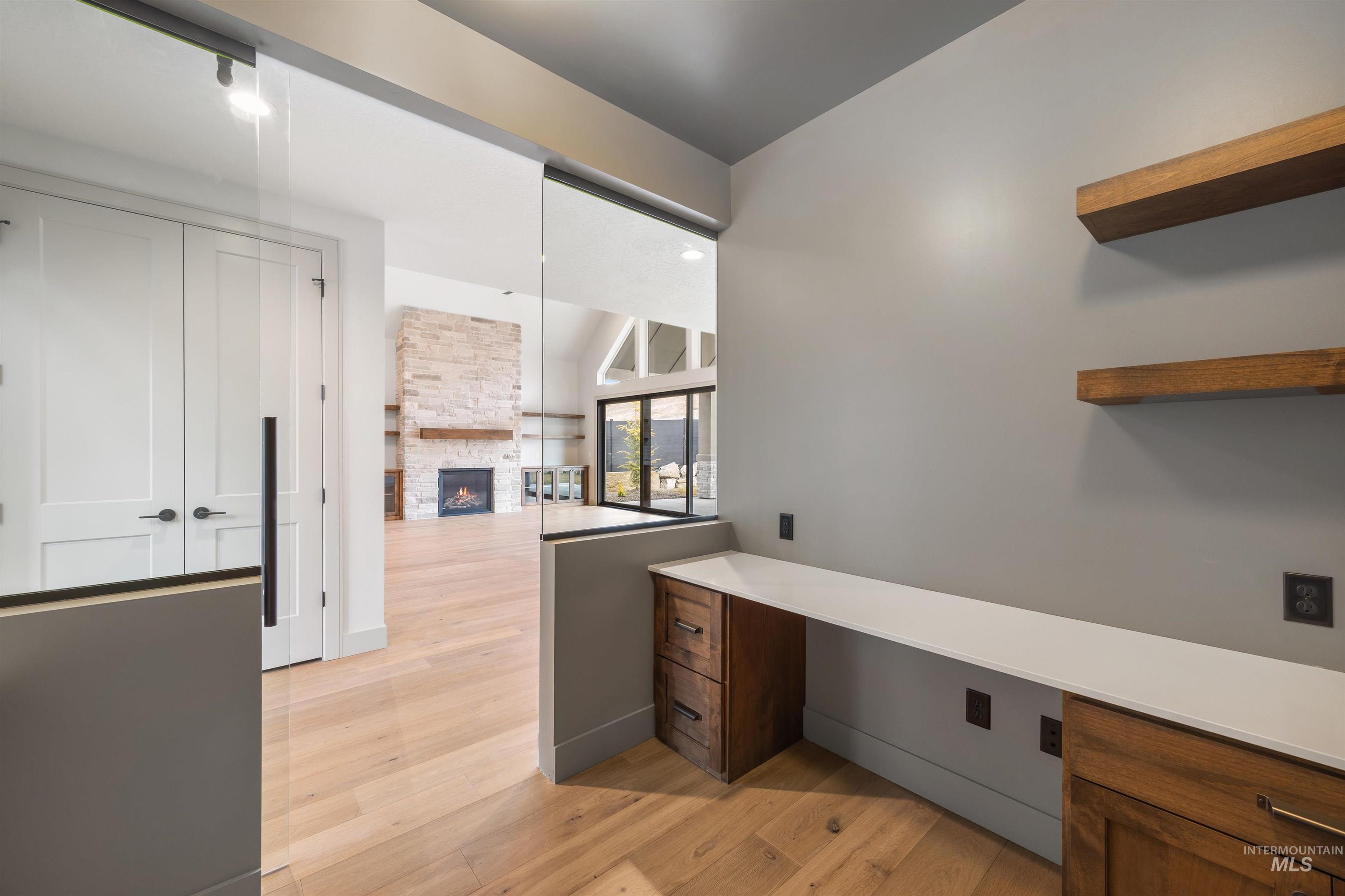 Unfurnished office featuring built in desk, a fireplace, light wood-style flooring, and vaulted ceiling