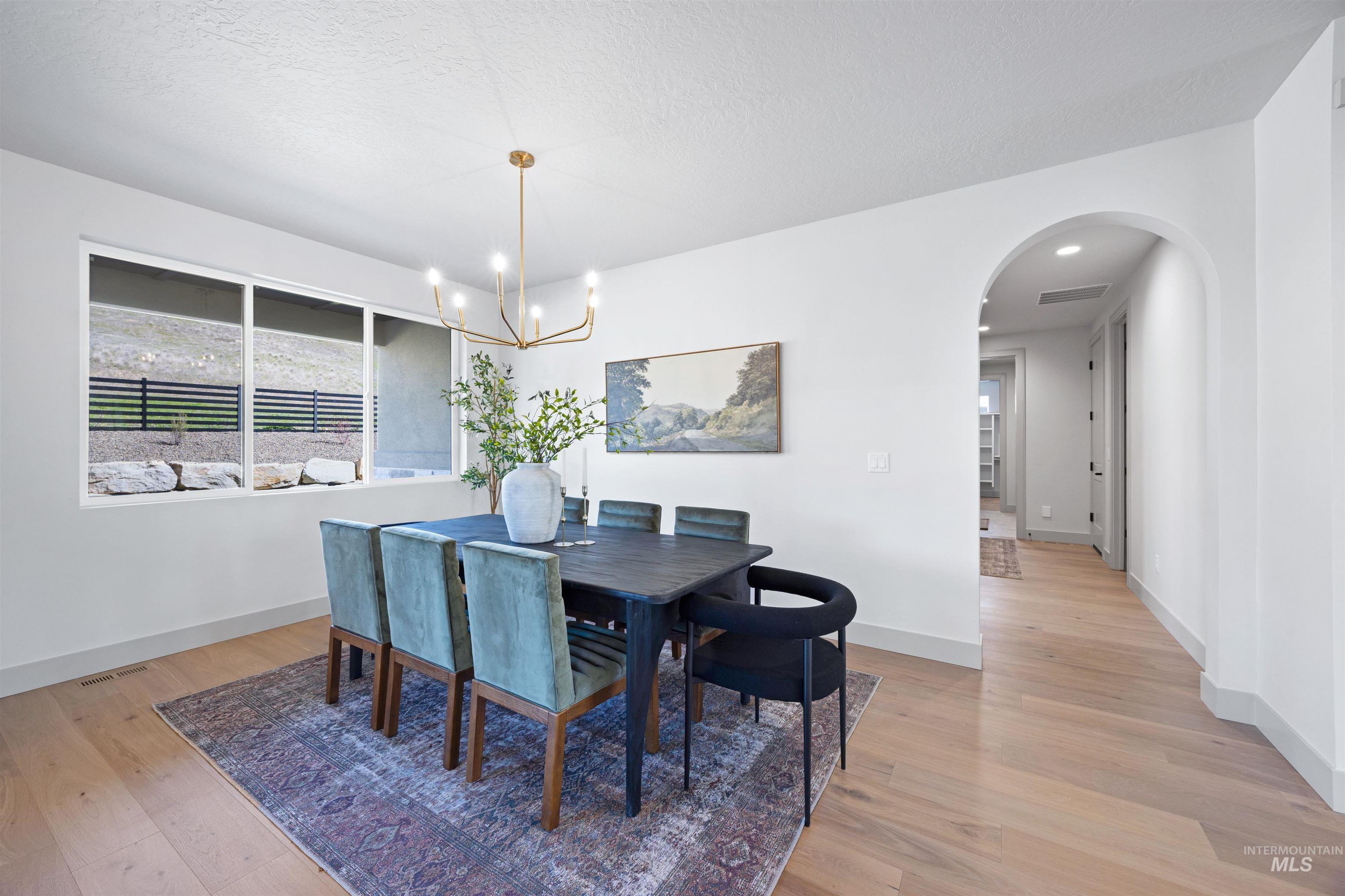 Dining area with arched walkways, light wood finished floors, hanging lights, and a textured ceiling
